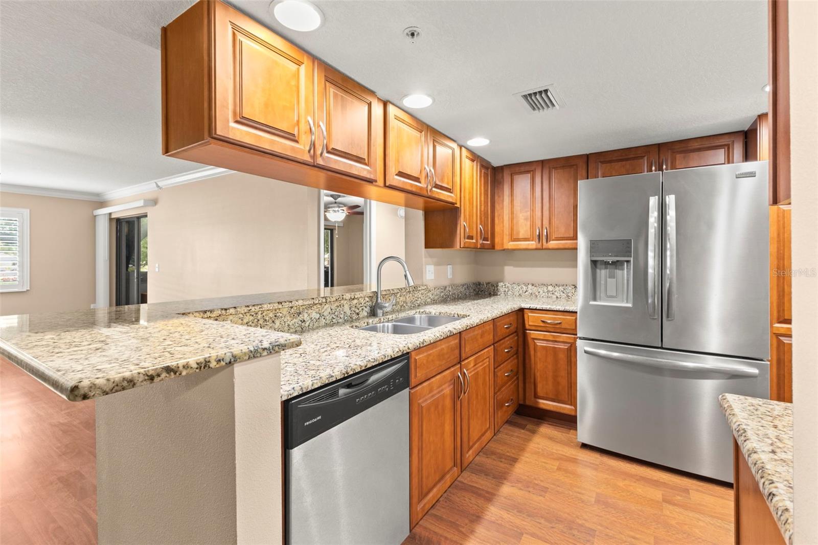 The open kitchen features granite countertops, extensive cabinet storage, stainless steel appliances, including a French-door refrigerator with water and ice dispensers, and a generous breakfast bar designed for both everyday use as well as entertaining.