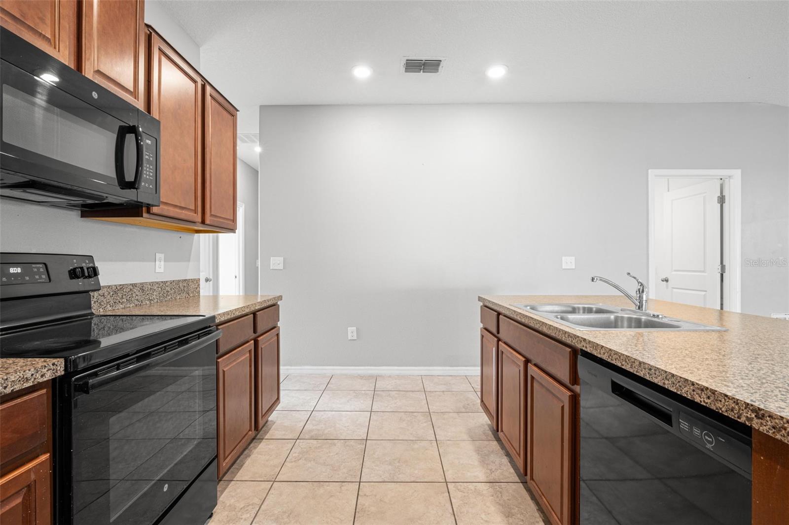 The oversized peninsula provides generous prep space, breakfast bar seating, and a double-basin stainless steel sink, creating a natural gathering place at the heart of the kitchen.
