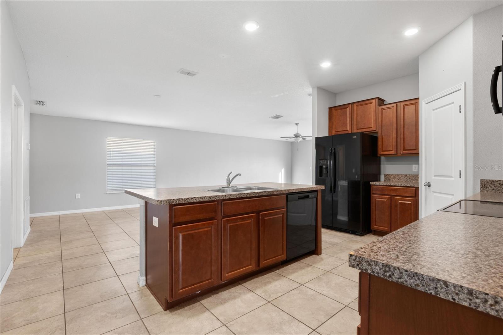 Kitchen with a double-basin stainless steel sink, granite countertops, black appliances, recessed lighting, tile flooring, and a peninsula with breakfast bar seating and cabinet storage.