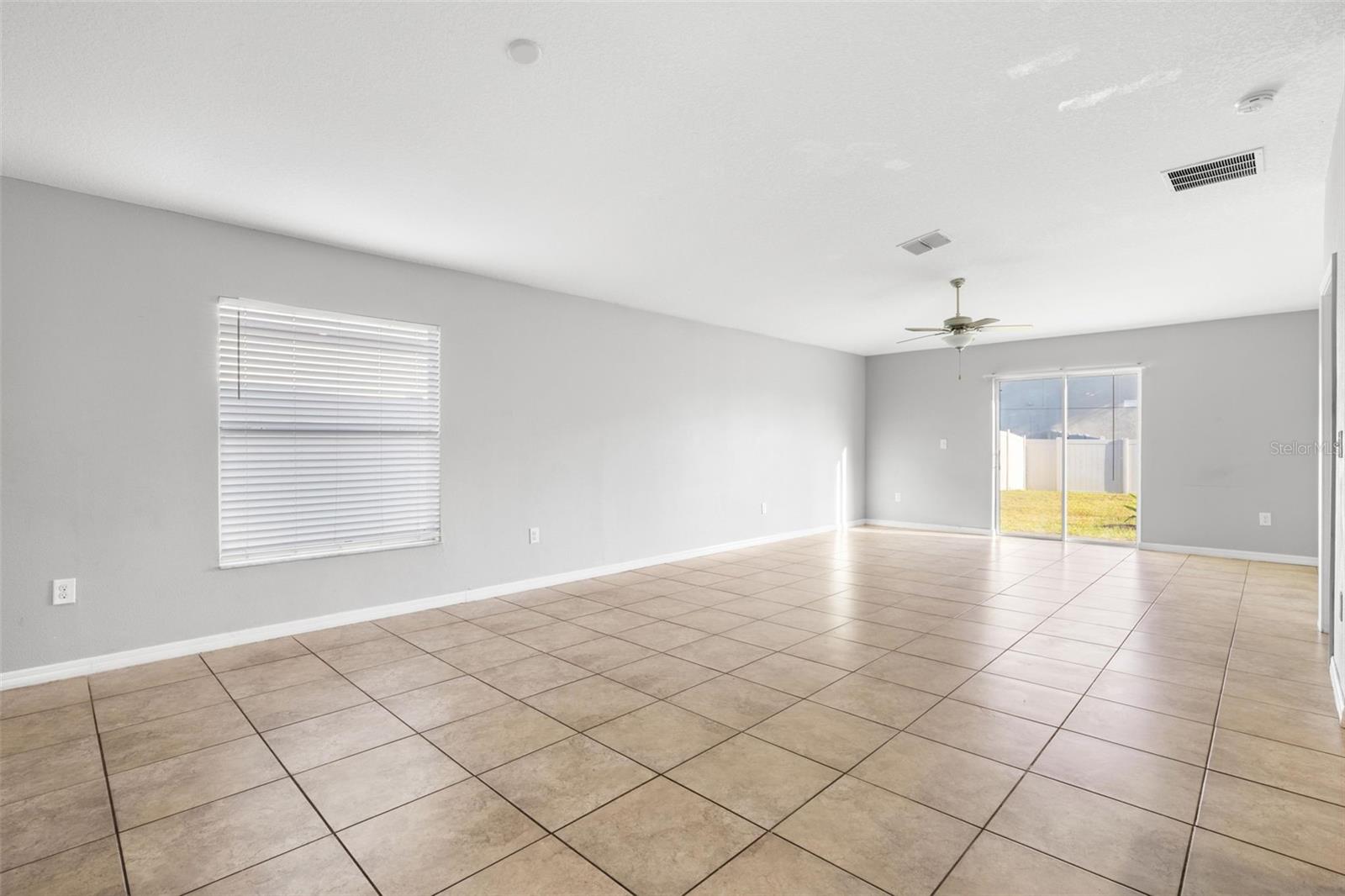Great room featuring ceramic tile flooring, ceiling fan, and sliding glass doors that open to a fenced backyard, filling the space with natural light.
