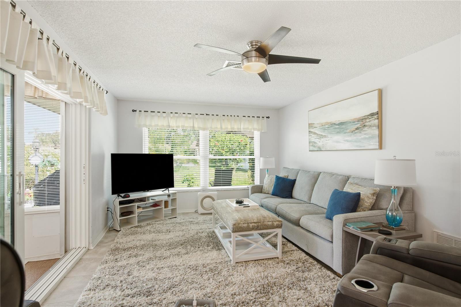 Cozu secondary living space highlighted by large windows, a modern ceiling fan, and sliding glass doors that lead out to a fully heated and cooled Florida Room.