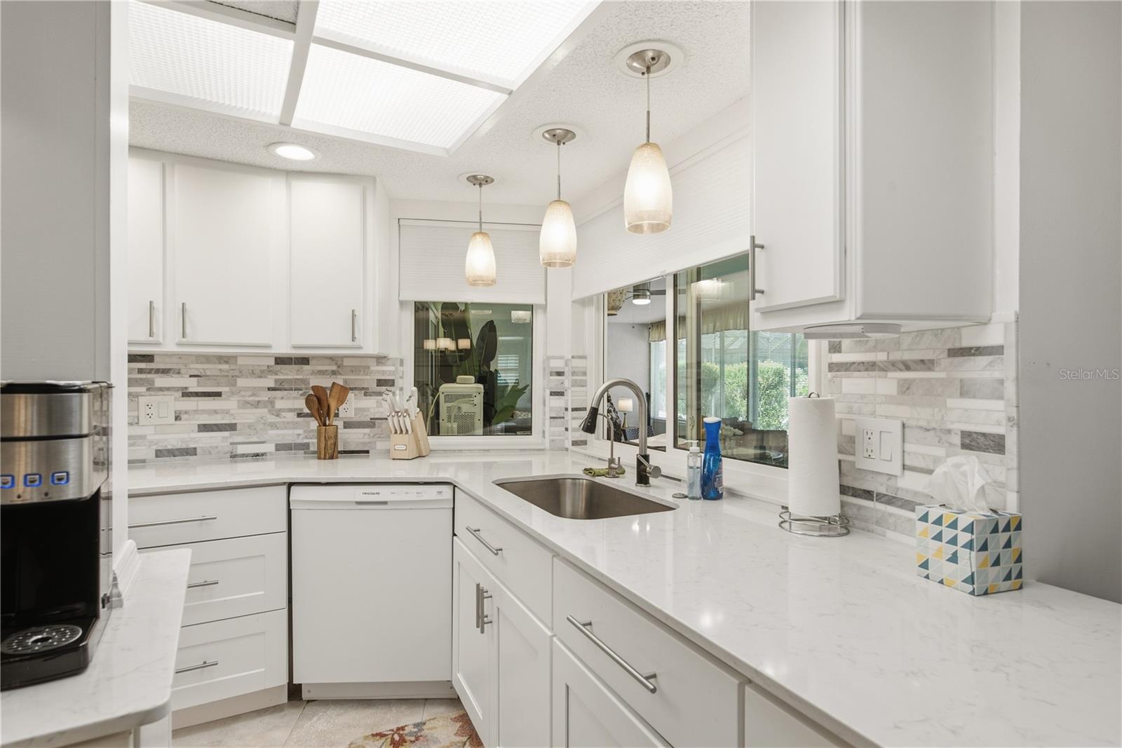Modern kitchen with crisp white cabinetry, beautiful stone countertops, a stylish tiled backsplash, and elegant lighting.