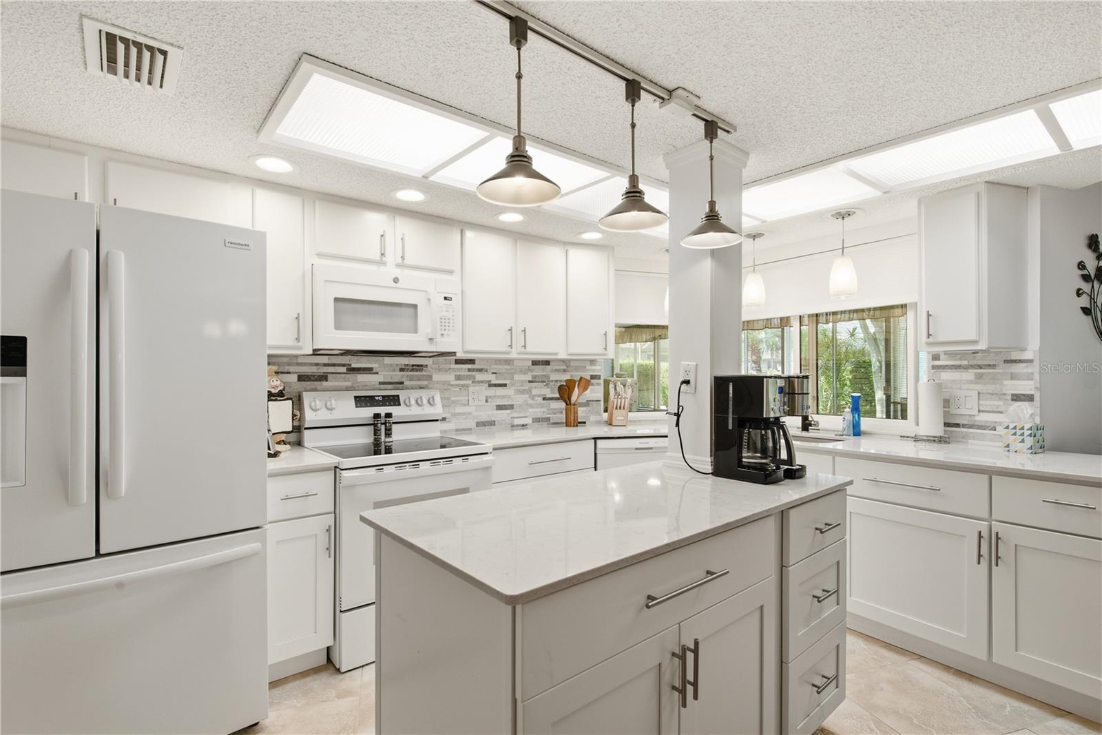 Spacious, updated kitchen featuring a functional center island, ample cabinet storage, matching white appliances, and sleek modern track lighting.