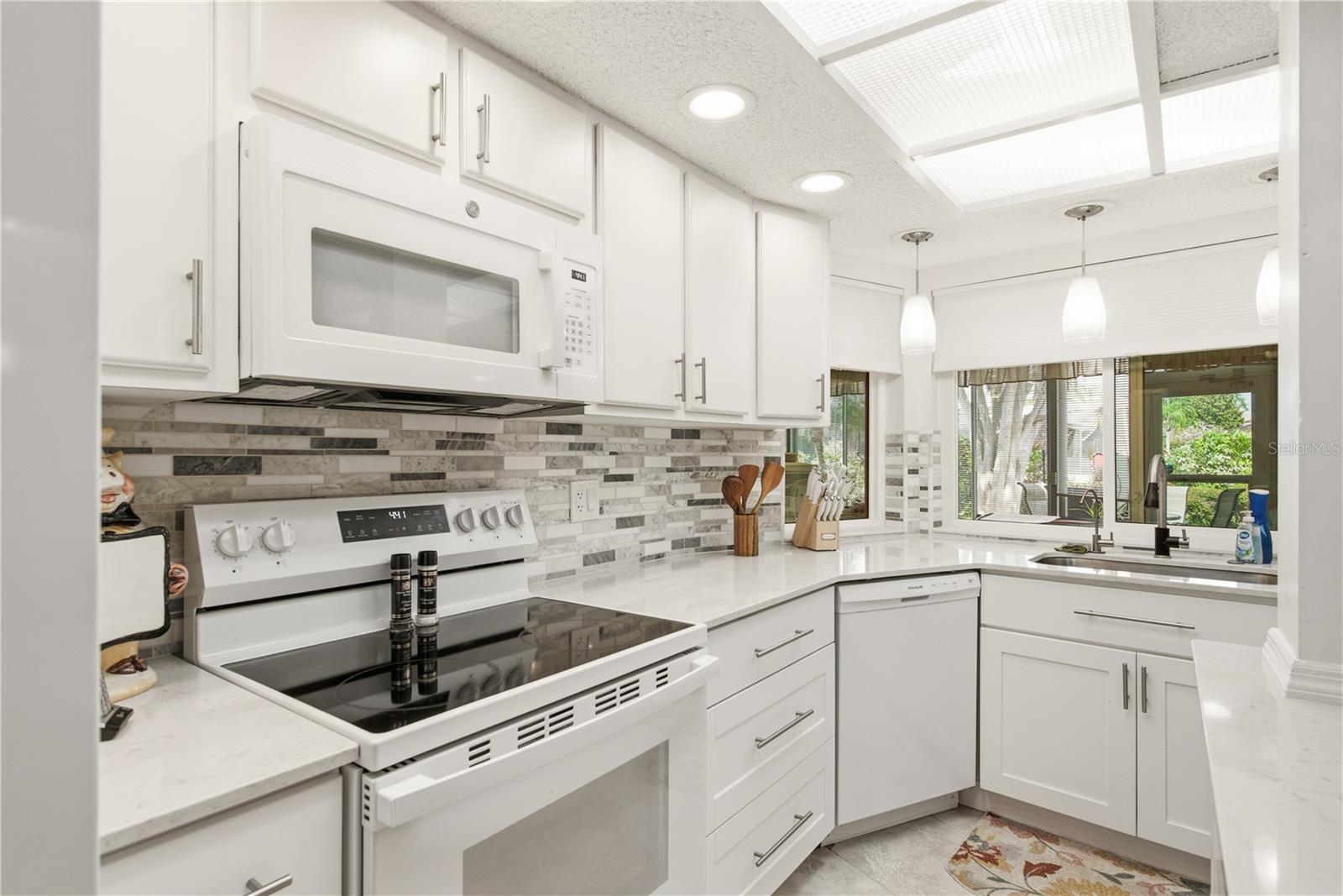 Sleek kitchen setup showcasing matching white appliances, a smooth glass top stove, modern tiled backsplash and built in lighting.