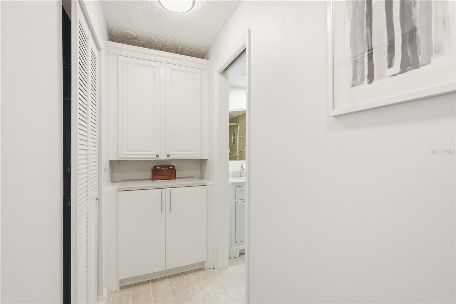 Primary suite hallway featuring custom built in cabinetry, with a his and her shared walk in closet to the left and the en suite bathroom to the right.