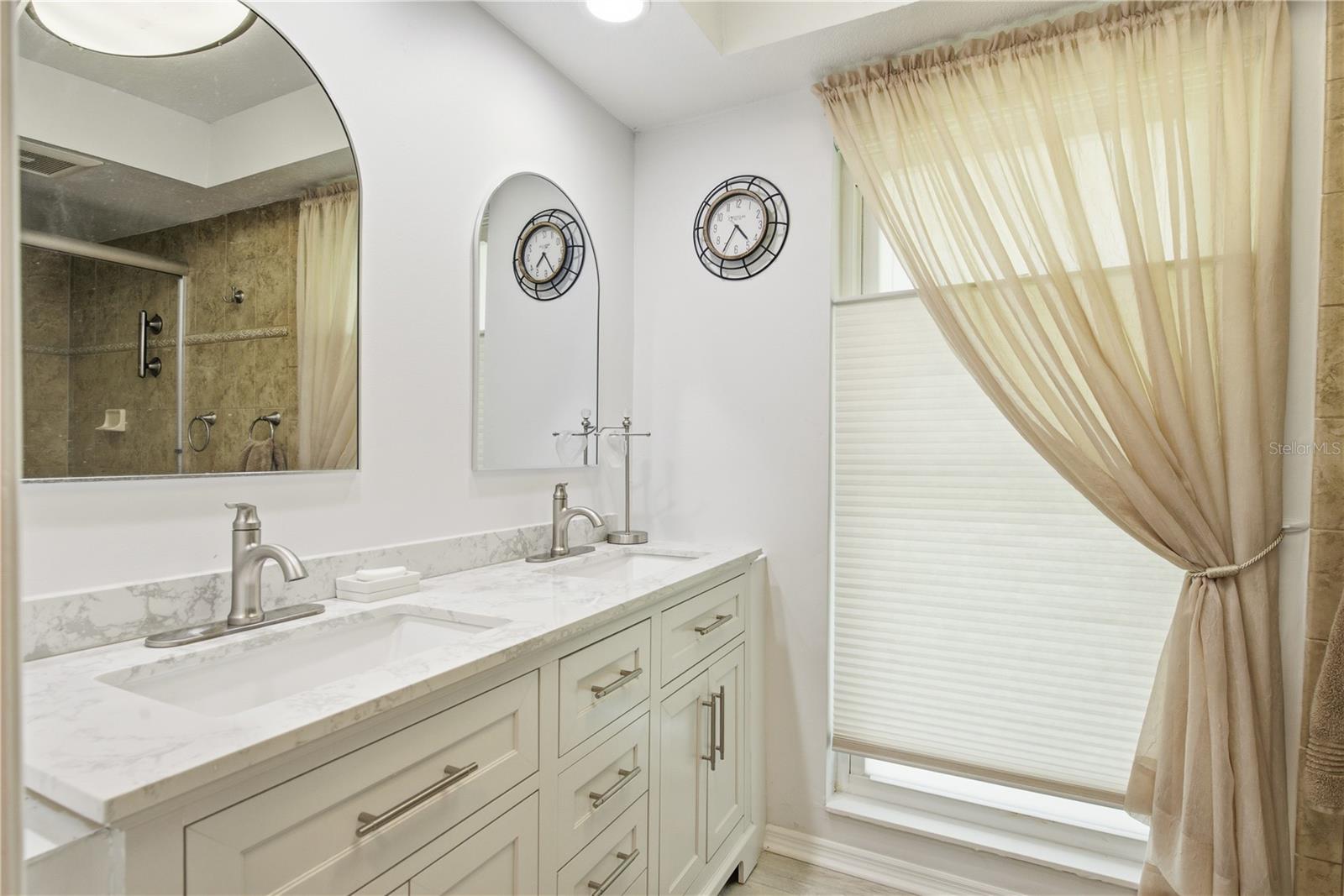Primary bathroom featuring a long double vanity with stone countertops, ample cabinet storage, modern hardware, and matching arched mirrors.