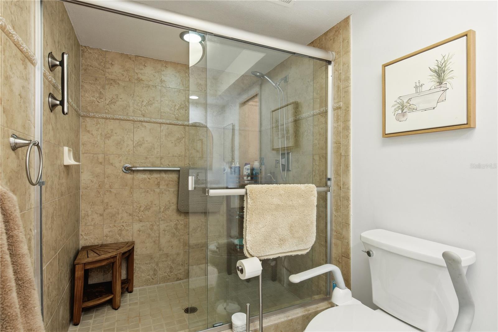 primary bathroom features a spacious walk in shower with floor to ceiling tile, glass sliding doors, integrated safety grab bars, and a handy corner seat.