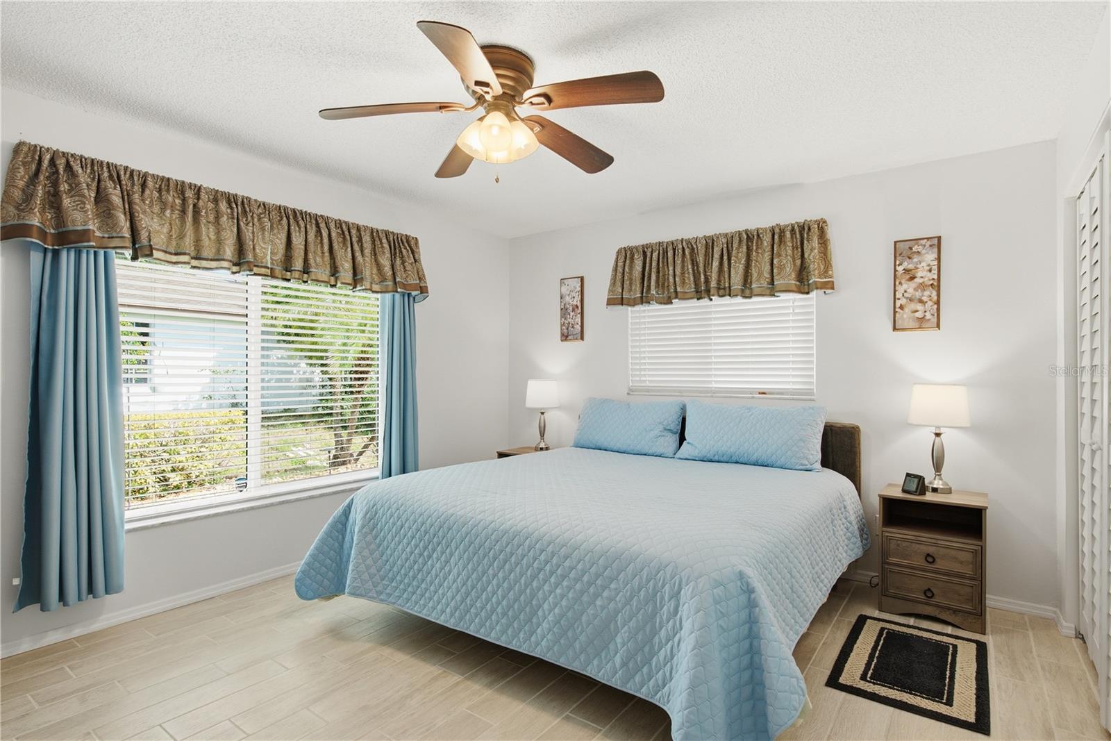 Bright and spacious bedroom featuring durable flooring, a lighted ceiling fan, and large hurricane proof windows that let plenty of natural light in.