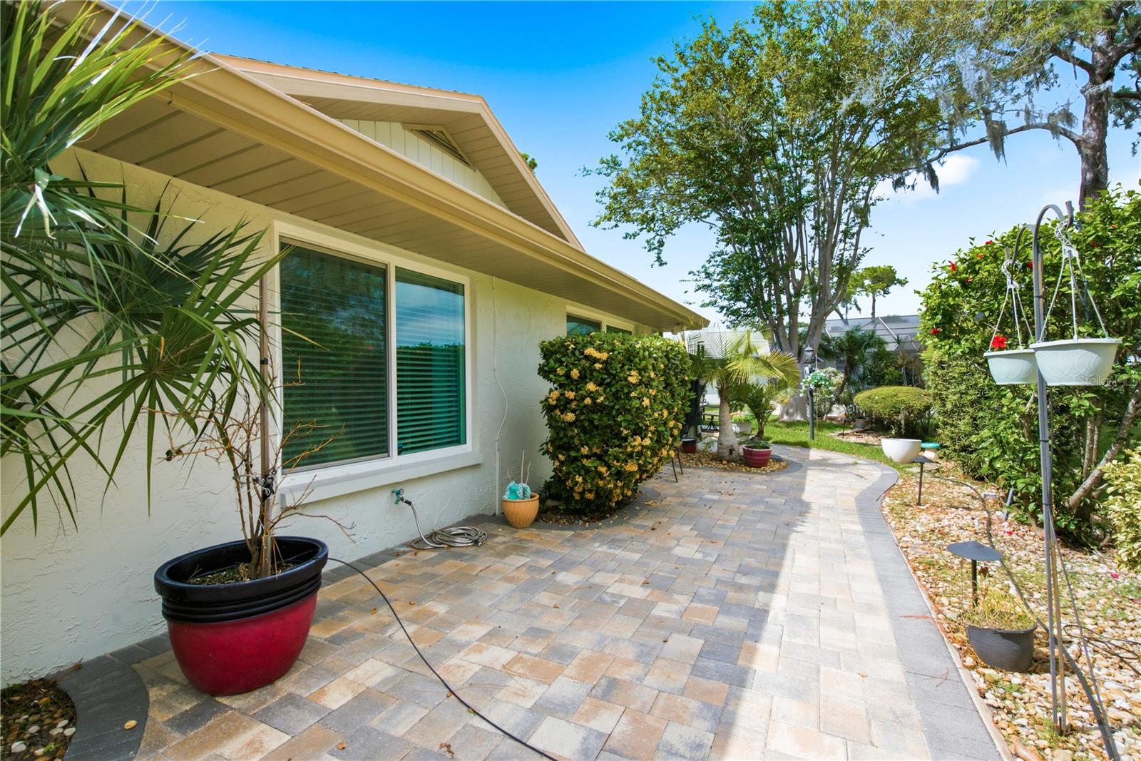 Continuation of the rear brick patio, showcasing the landscape walkway wrapping around the side of the home with manicured garden beds.