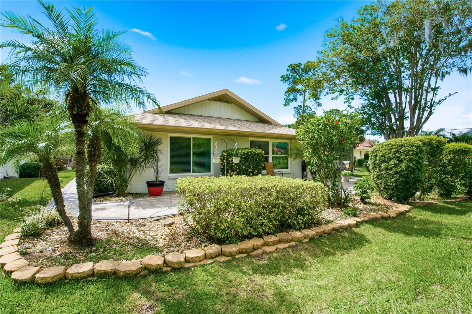 Zoomed out view of the rear exterior, highlighting beautifully manicured garden beds with stone curbing, a mature palm tree, and lush green lawn.