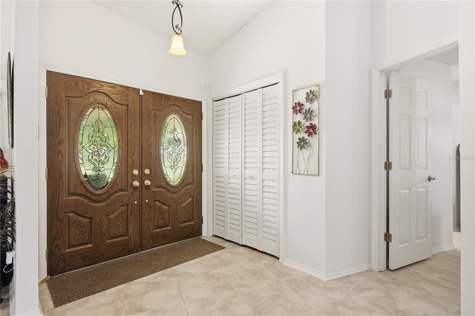 Step inside to a bright, welcoming foyer featuring elegant double front doors with decorative glass and high ceilings.