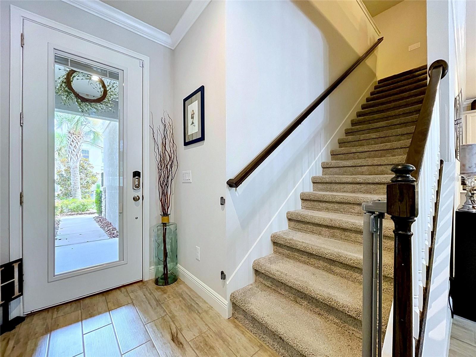 Step inside and immediately feel at home. This welcoming entry features wood-look tile flooring, crown molding, abundant natural light, and a dramatic staircase with dark wood accents that creates a warm and elegant first impression.