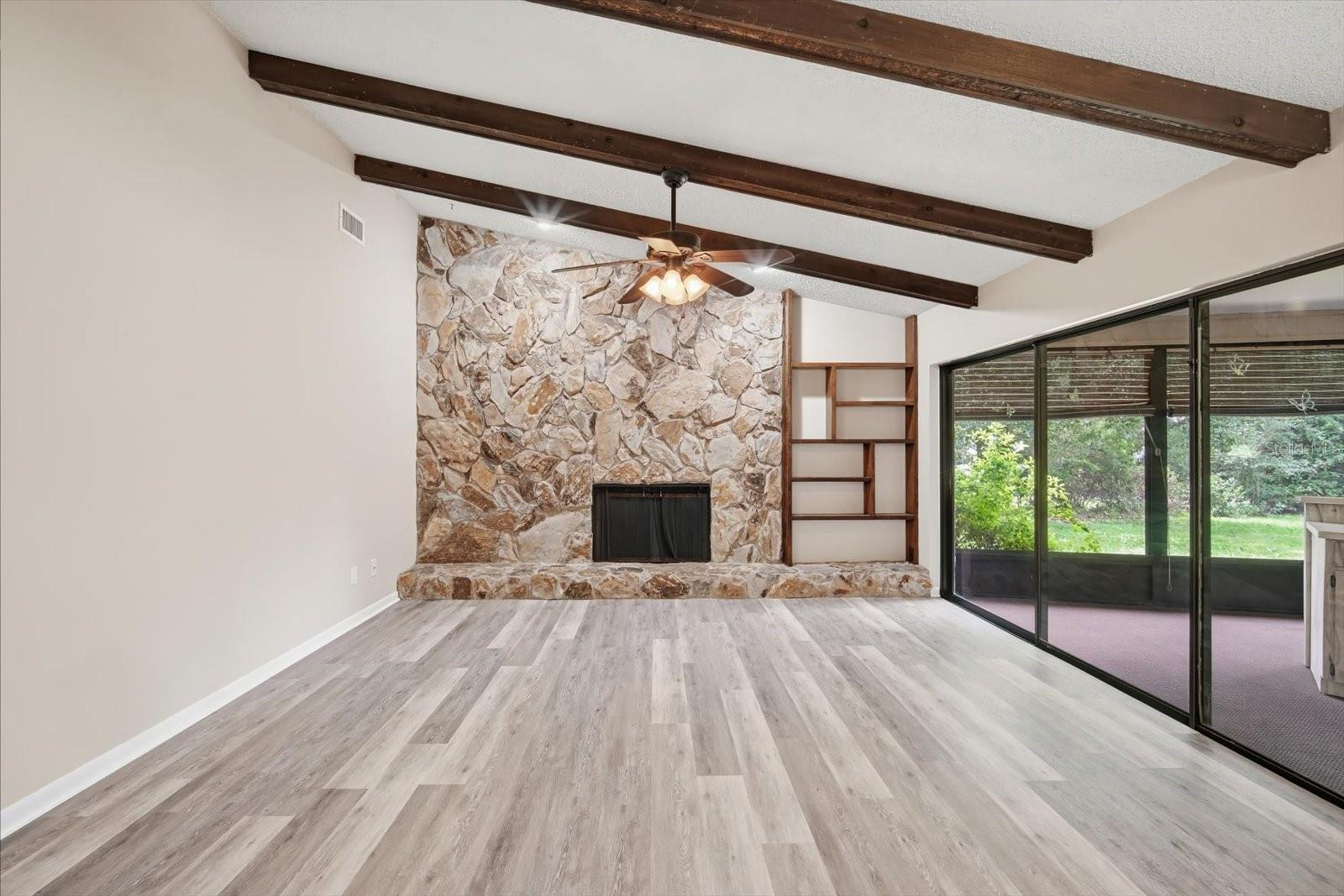 Impressive family room with soaring ceilings with stone fireplace, beams and triple sliding glass doors