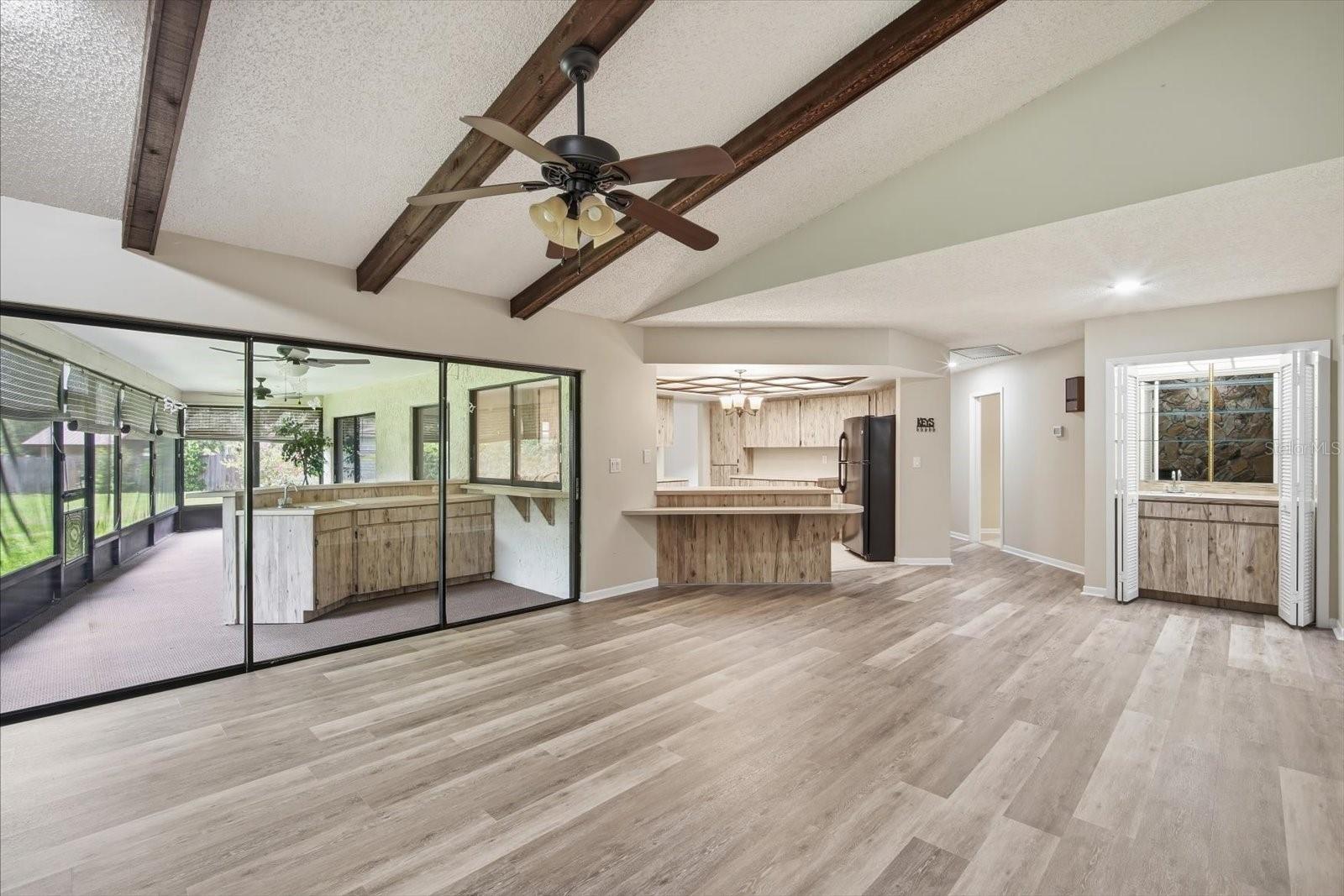 Impressive family room with soaring ceilings with stone fireplace, beams and triple sliding glass doors
