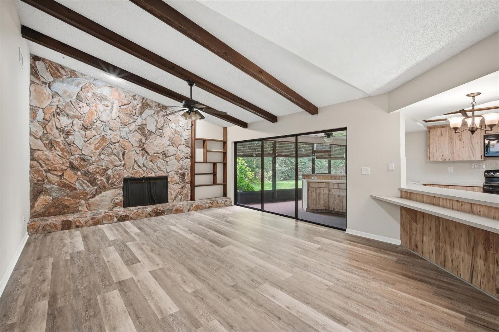 Impressive family room with soaring ceilings with stone fireplace, beams and triple sliding glass doors