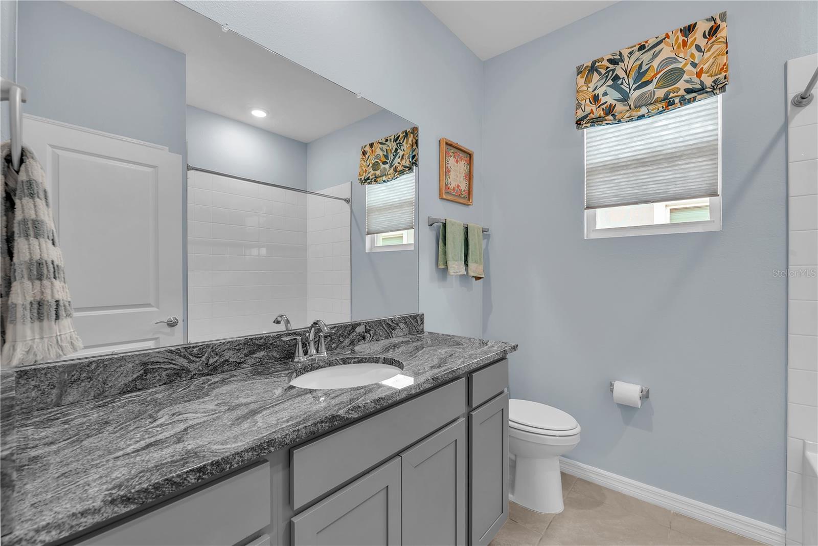 Guest bathroom has a tub/shower combination and a large vanity with storage topped with granite counter top.