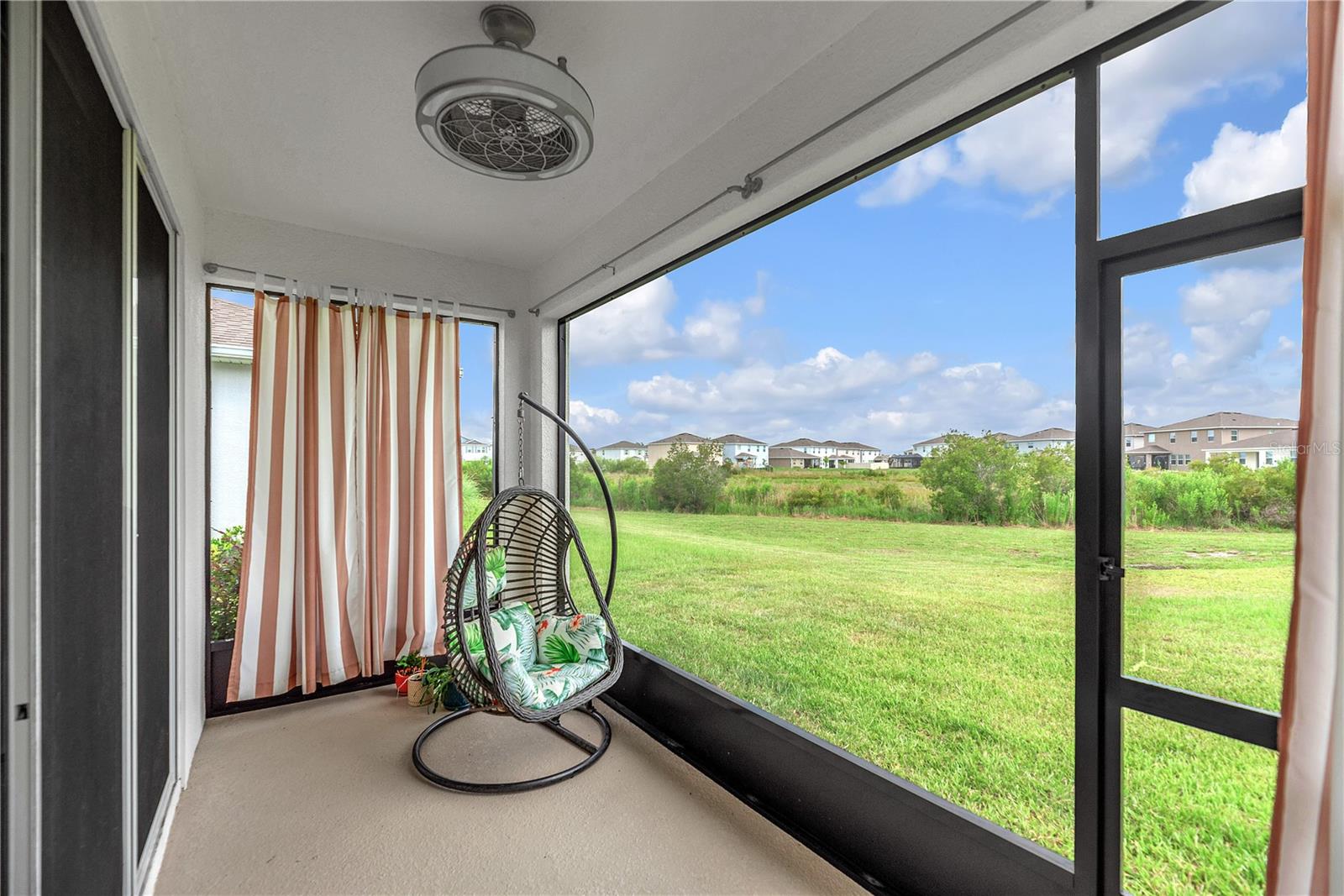 The covered and screened lanai with fan looks out over a green space, creating the perfect outdoor retreat for relaxing, entertaining, or spending quality time with family and pets