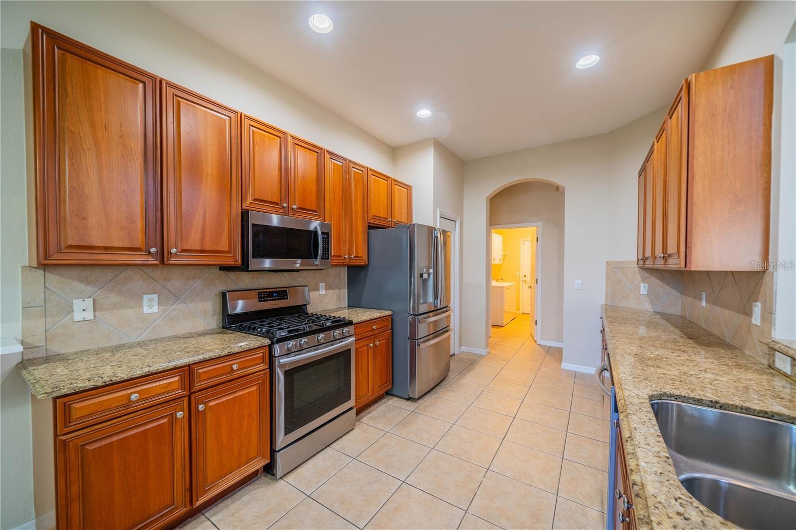Kitchen features warm wood cabinets, a gas stove, and elegant granite countertops.
