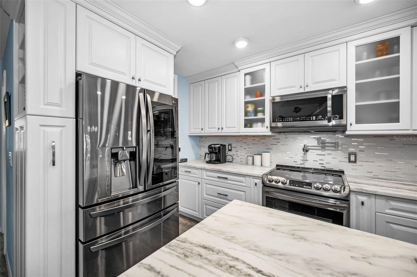 Refined glass-panel cabinetry, marble countertops and subway tile backsplash that elevates the kitchen’s coastal-contemporary aesthetic