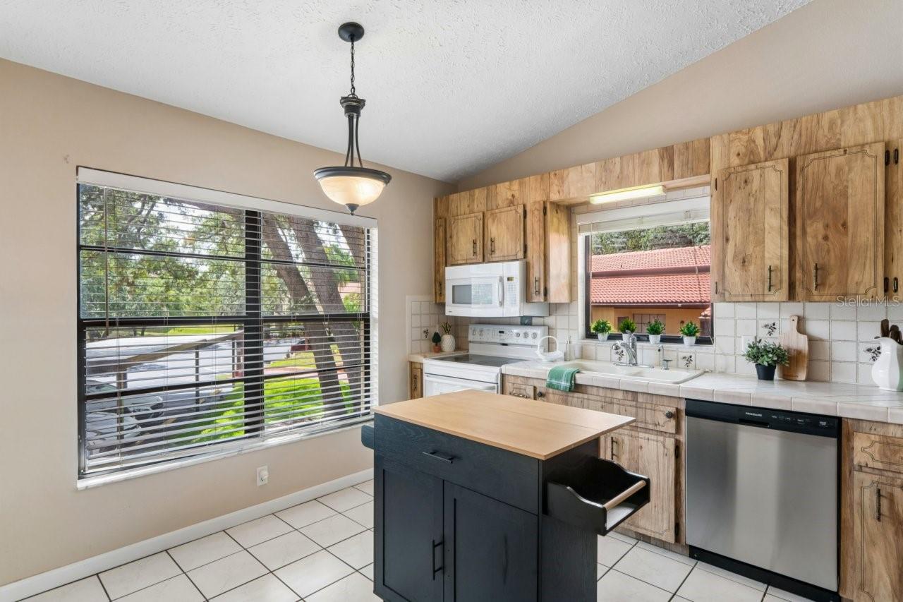 The kitchen has ceramic tile flooring, double porcelain sink, brand new dishwasher, range, microwave, portable center island, and ceramic tiled counters.