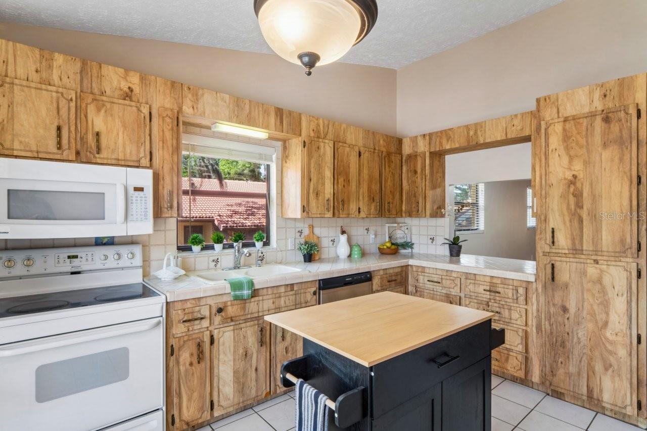 Kitchen has a pass-through breakfast bar, bright window and wood cabinets and pantry cabinet.