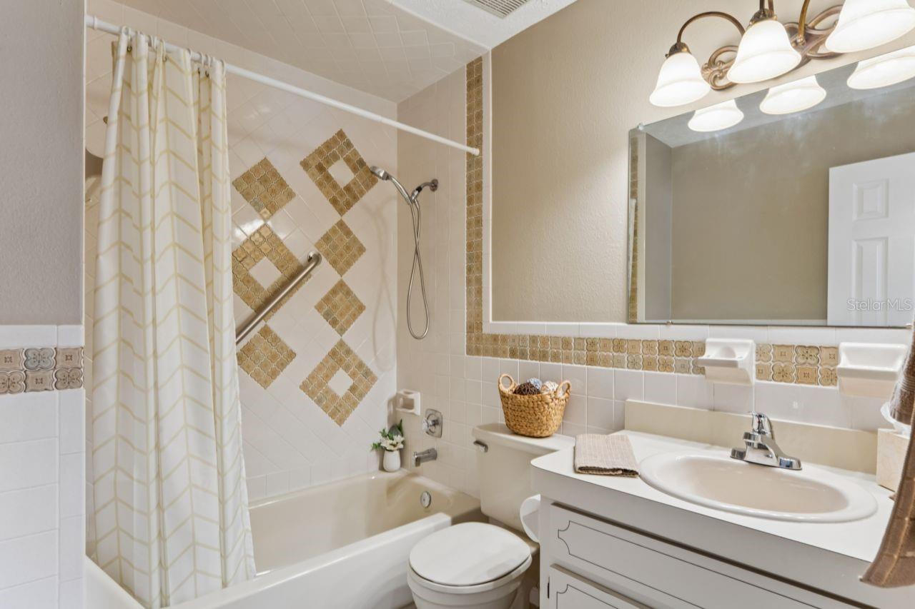 Guest bathroom has a bathtub with shower, single vanity and a newer light fixture with a large mirror.
