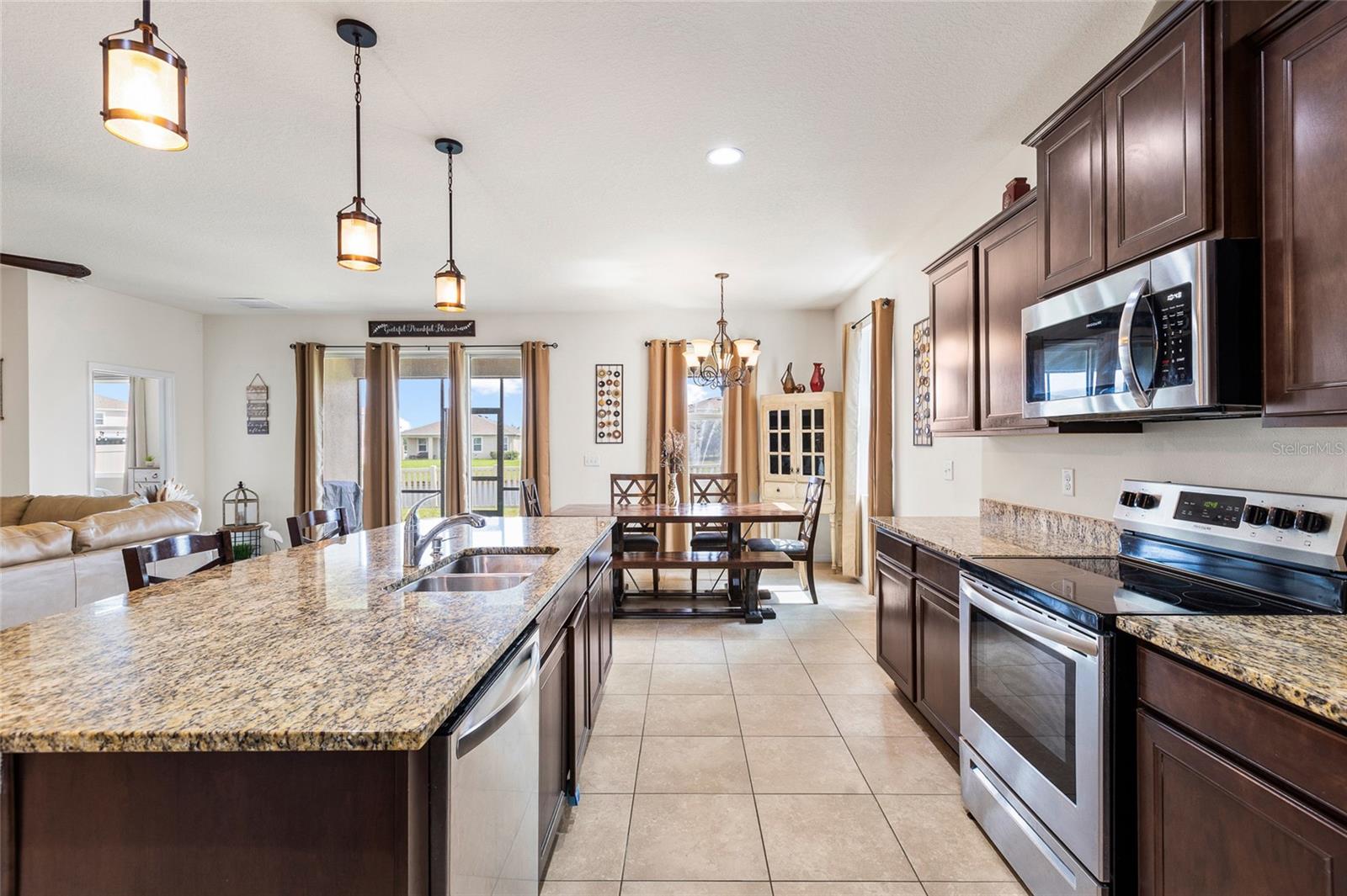 The heart of the home is the spacious open-concept kitchen, designed for both everyday living and entertaining. Features include granite countertops, a large center island with breakfast bar seating, stainless steel appliances, 36-inch cabinetry, a corner pantry, and abundant counter space. The kitchen seamlessly connects to the dining and living areas, creating a bright and functional gathering space.