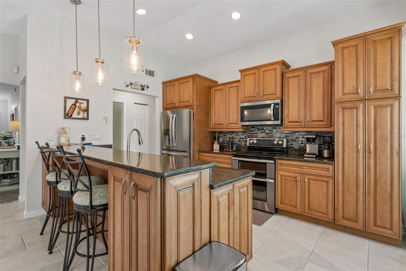 The eat-in kitchen is beautifully appointed with stainless steel appliances, granite countertops, breakfast bar seating, cabinet pullouts, soft-close drawers, and a cheerful breakfast nook surrounded by windows.