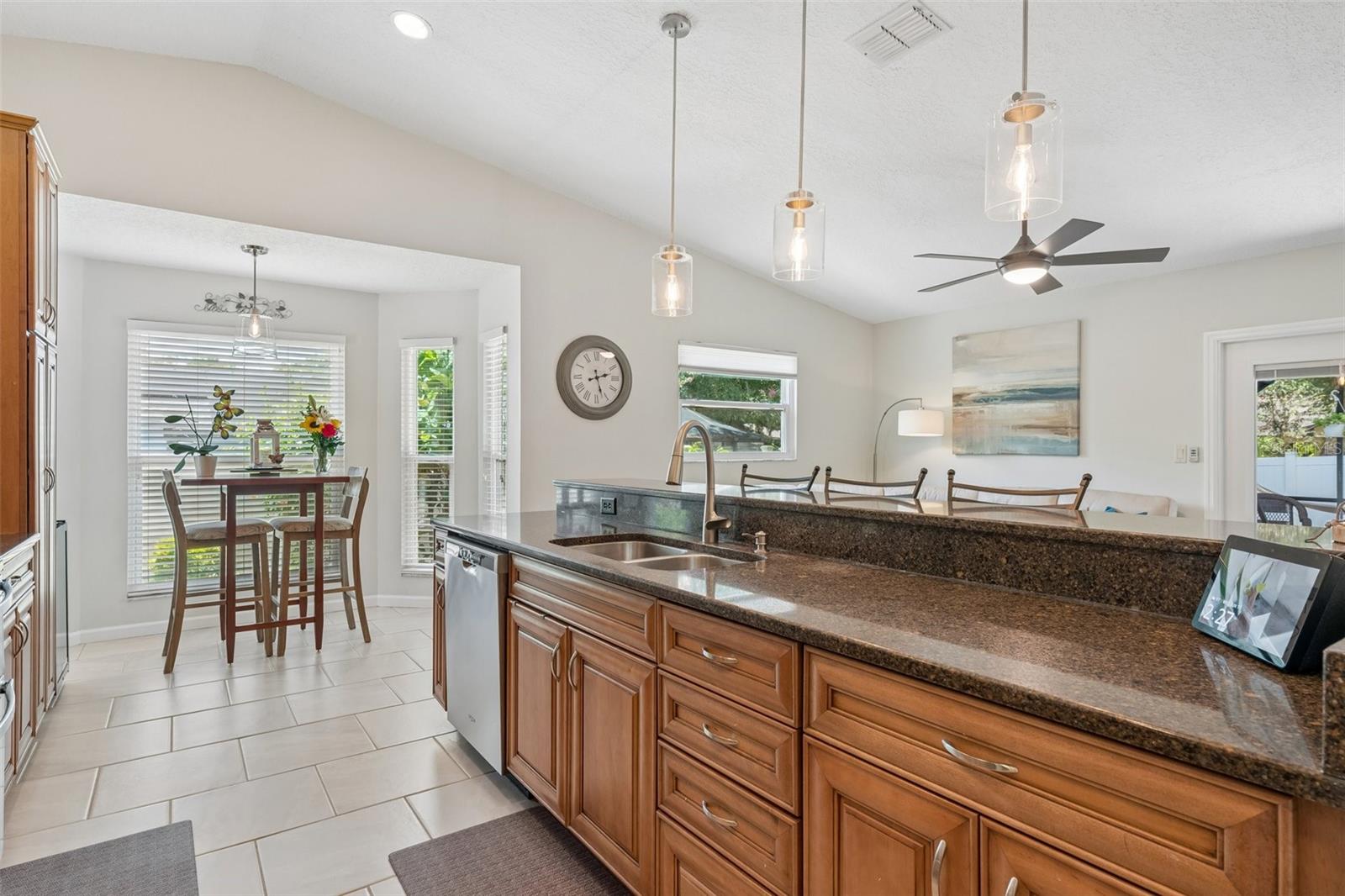 The eat-in kitchen is beautifully appointed with stainless steel appliances, granite countertops, breakfast bar seating, cabinet pullouts, soft-close drawers, and a cheerful breakfast nook surrounded by windows.