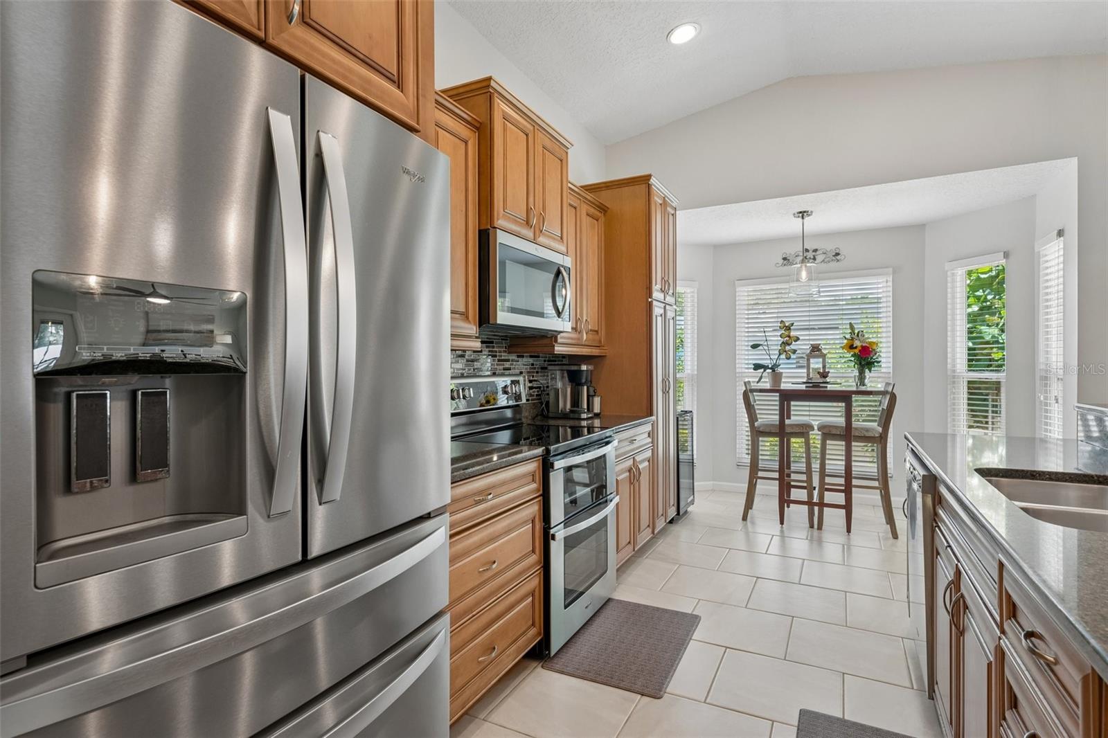 The eat-in kitchen is beautifully appointed with stainless steel appliances, granite countertops, breakfast bar seating, cabinet pullouts, soft-close drawers, and a cheerful breakfast nook surrounded by windows.