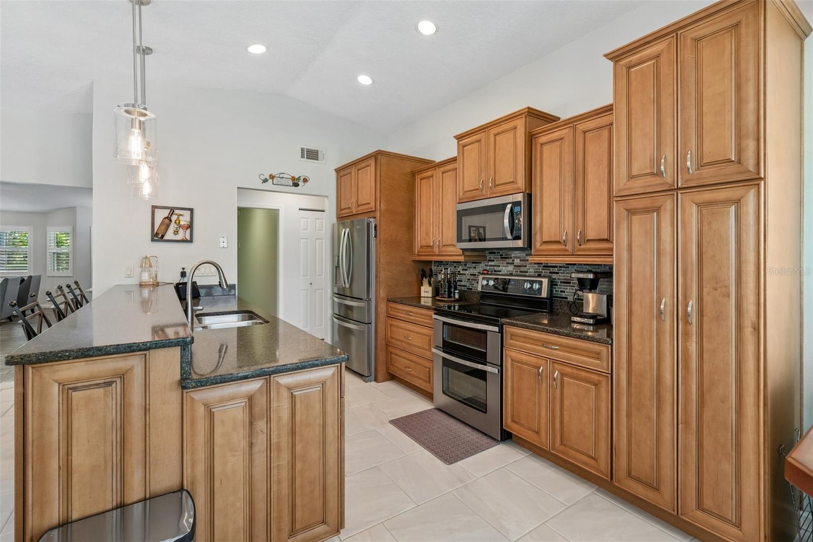 The eat-in kitchen is beautifully appointed with stainless steel appliances, granite countertops, breakfast bar seating, cabinet pullouts, soft-close drawers, and a cheerful breakfast nook surrounded by windows.