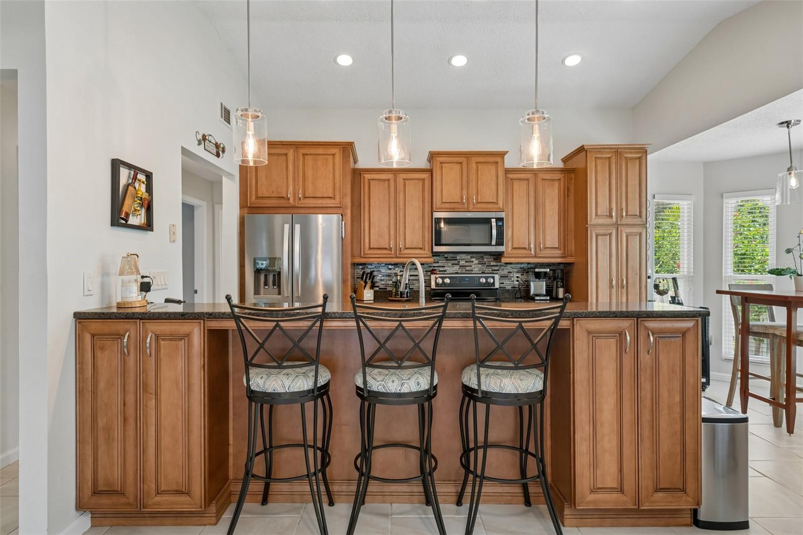 The eat-in kitchen is beautifully appointed with stainless steel appliances, granite countertops, breakfast bar seating, cabinet pullouts, soft-close drawers, and a cheerful breakfast nook surrounded by windows.