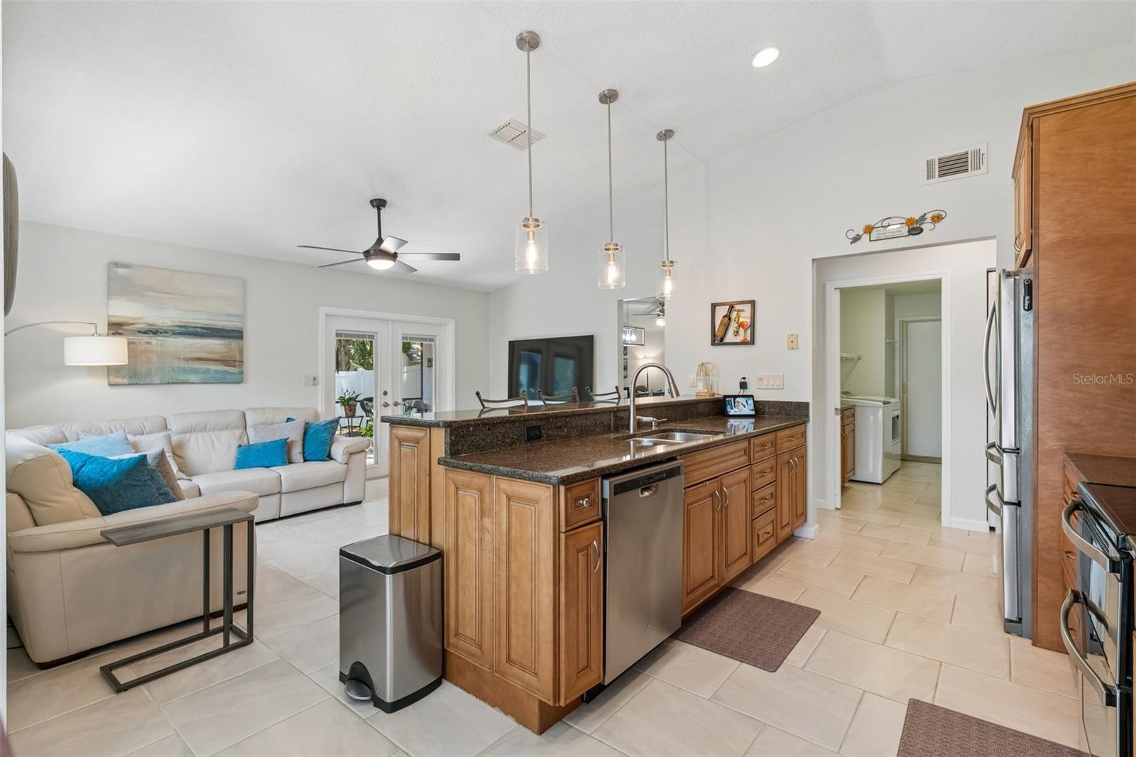 The kitchen opens to the family room, creating a connected everyday living space with tile flooring, vaulted ceilings, and French doors leading out to the patio.