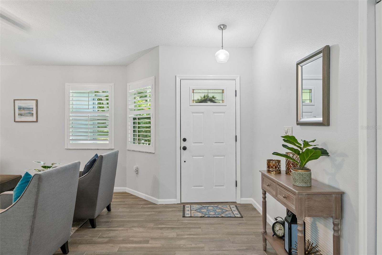 Living room with vaulted ceilings, wood-look tile floors, plantation shutters, and views out to the patio.