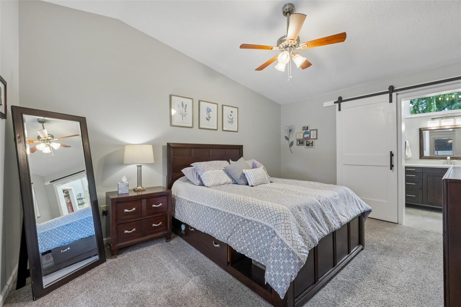 The primary bedroom is set on its own side of the home with vaulted ceilings, French doors to the patio, and an updated ensuite bath featuring a custom vanity, beautifully tiled glass-enclosed stand-up shower, high arched window, and walk-in closet with organized storage