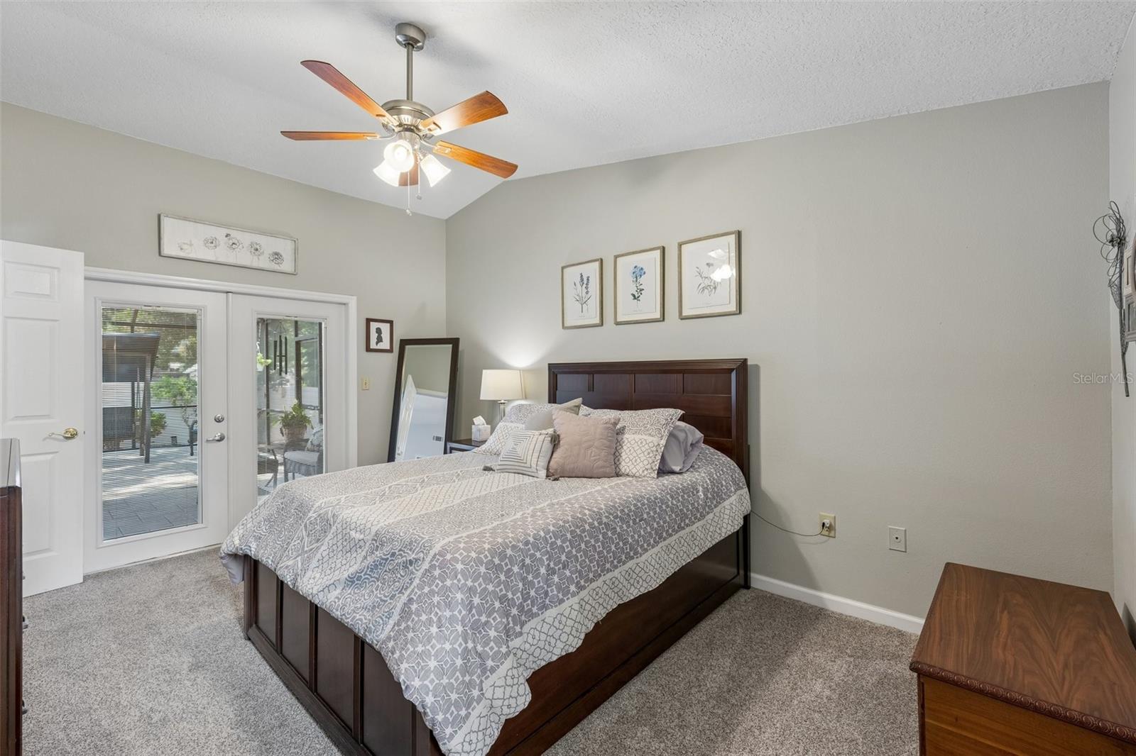 The primary bedroom is set on its own side of the home with vaulted ceilings, French doors to the patio, and an updated ensuite bath featuring a custom vanity, beautifully tiled glass-enclosed stand-up shower, high arched window, and walk-in closet with organized storage