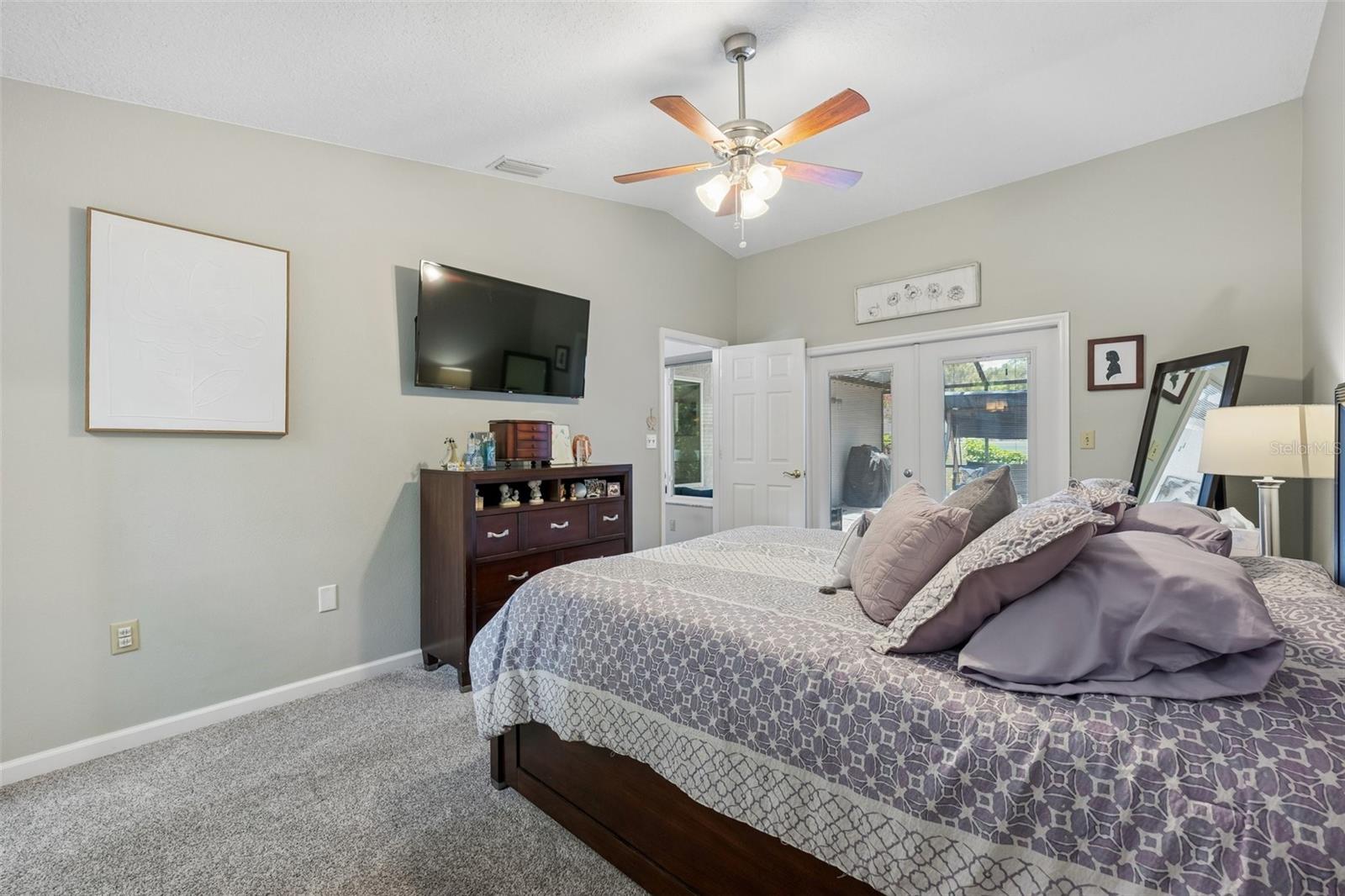 The primary bedroom is set on its own side of the home with vaulted ceilings, French doors to the patio, and an updated ensuite bath featuring a custom vanity, beautifully tiled glass-enclosed stand-up shower, high arched window, and walk-in closet with organized storage