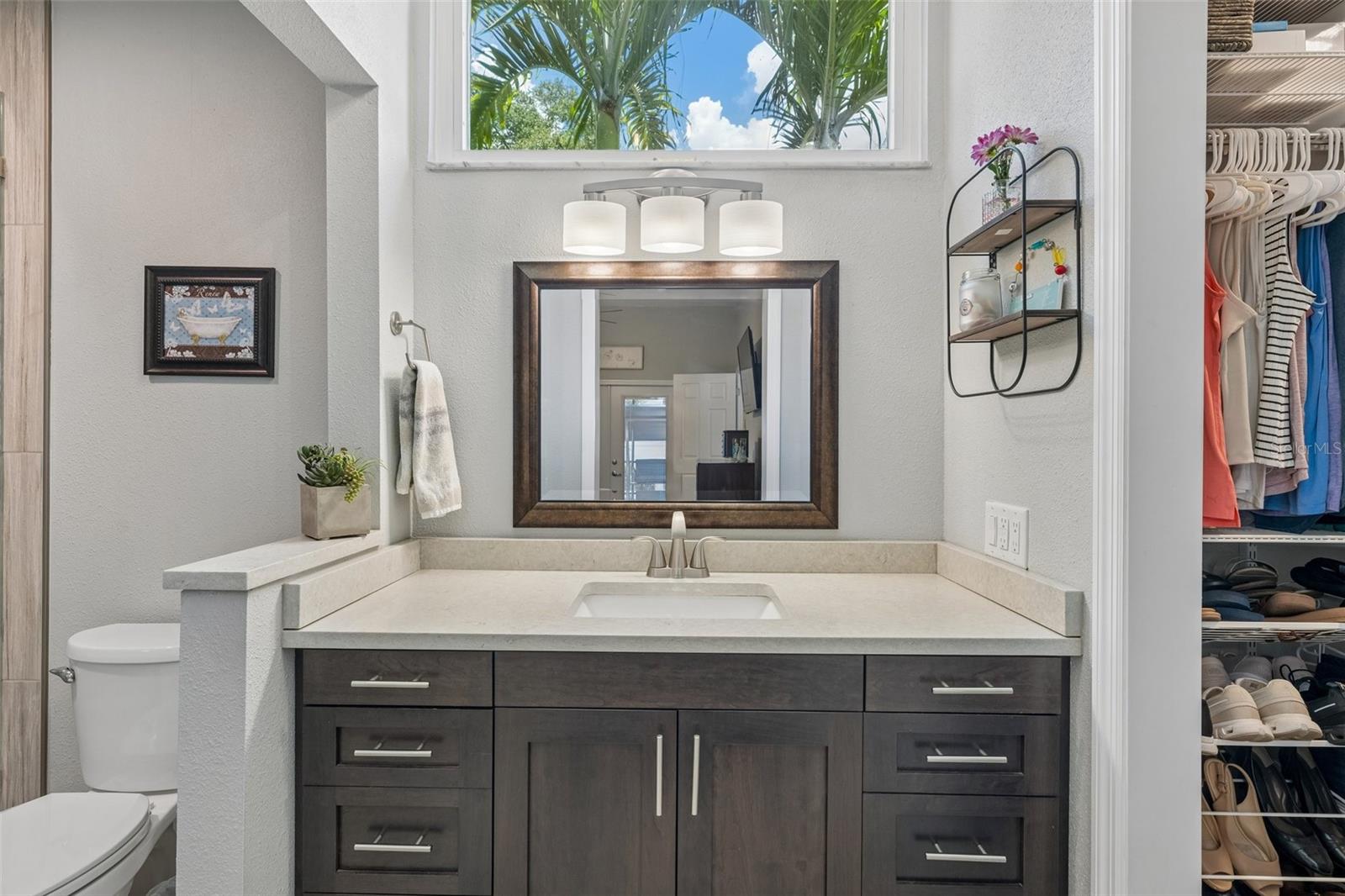 The primary bedroom is set on its own side of the home with vaulted ceilings, French doors to the patio, and an updated ensuite bath featuring a custom vanity, beautifully tiled glass-enclosed stand-up shower, high arched window, and walk-in closet with organized storage