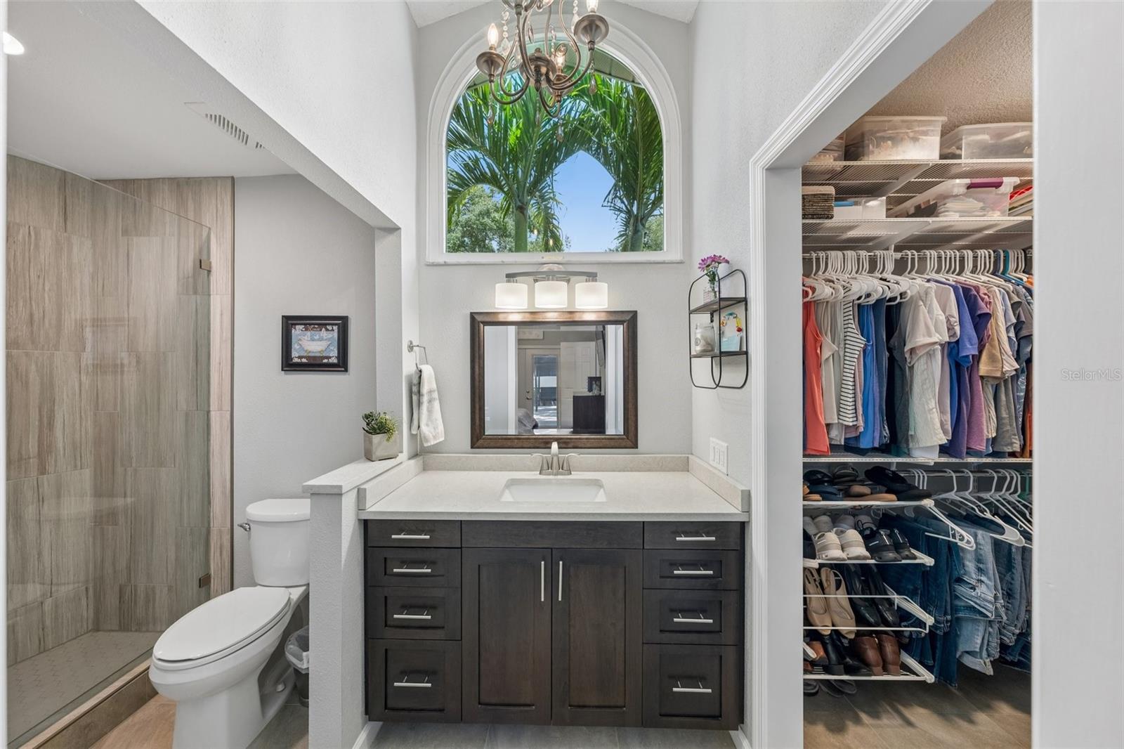 The primary bedroom is set on its own side of the home with vaulted ceilings, French doors to the patio, and an updated ensuite bath featuring a custom vanity, beautifully tiled glass-enclosed stand-up shower, high arched window, and walk-in closet with organized storage