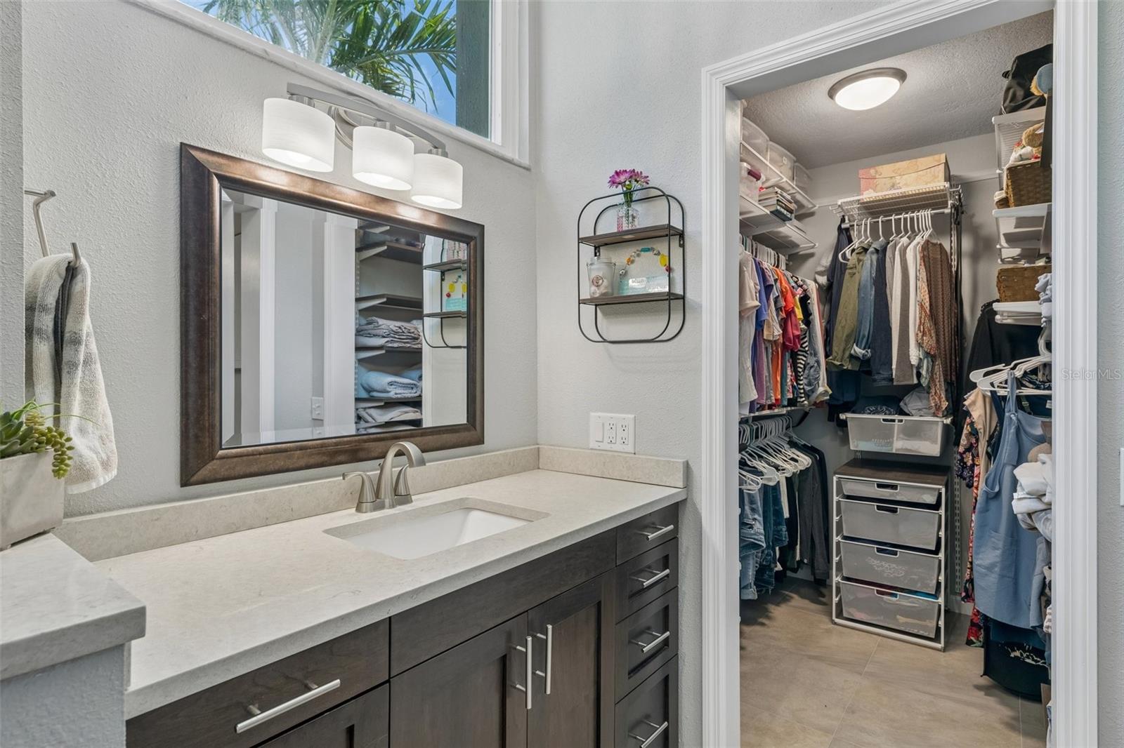 The primary bedroom is set on its own side of the home with vaulted ceilings, French doors to the patio, and an updated ensuite bath featuring a custom vanity, beautifully tiled glass-enclosed stand-up shower, high arched window, and walk-in closet with organized storage