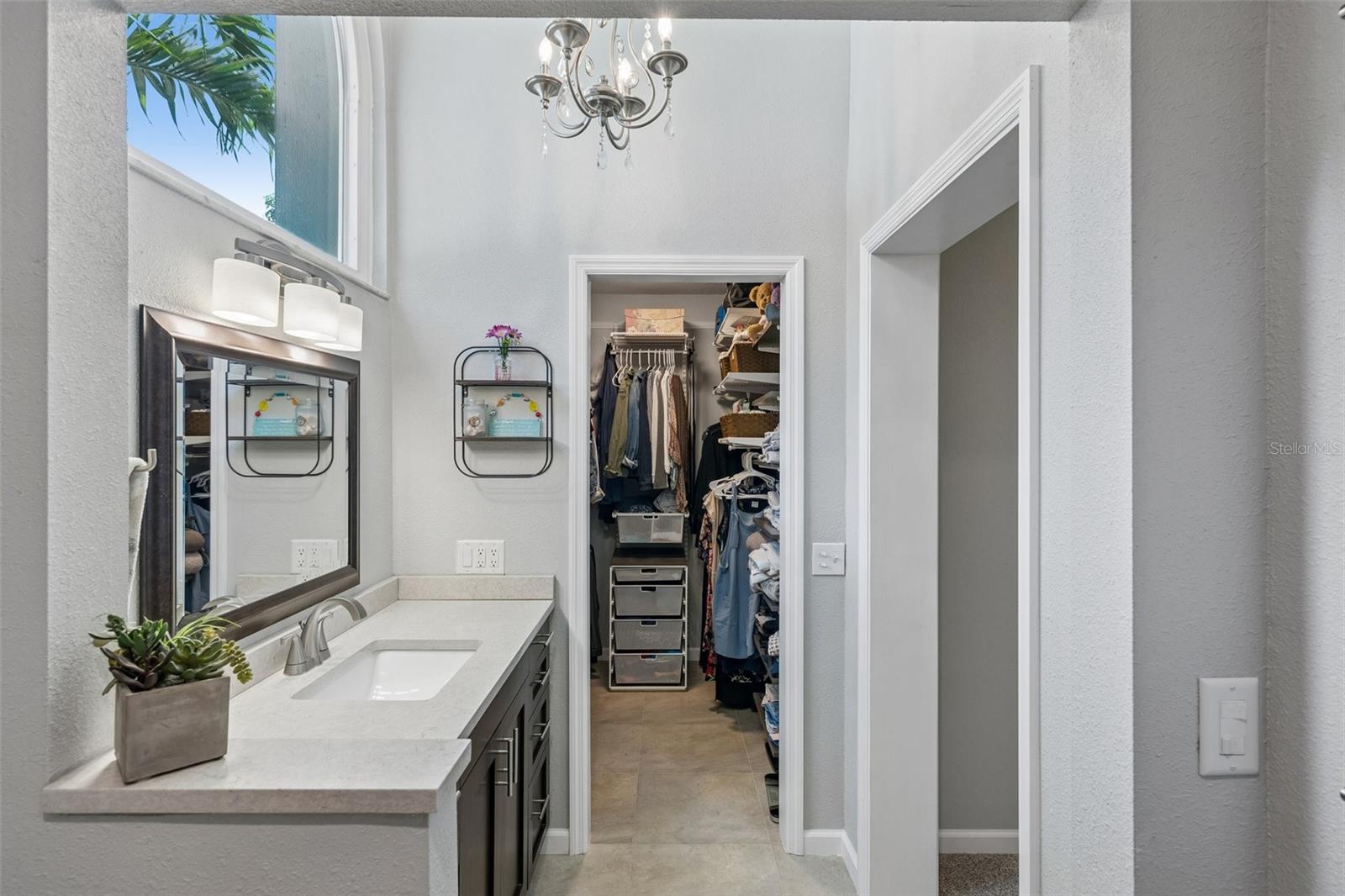 The primary bedroom is set on its own side of the home with vaulted ceilings, French doors to the patio, and an updated ensuite bath featuring a custom vanity, beautifully tiled glass-enclosed stand-up shower, high arched window, and walk-in closet with organized storage