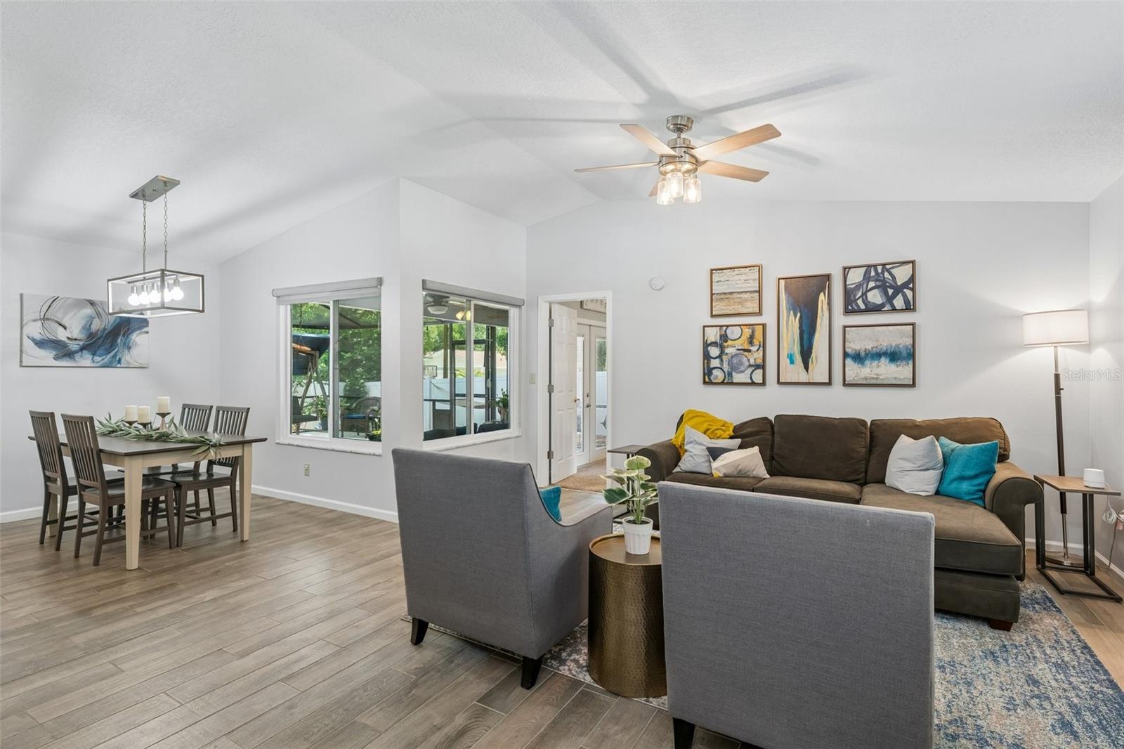 Living room with vaulted ceilings, wood-look tile floors, plantation shutters, and views out to the patio.