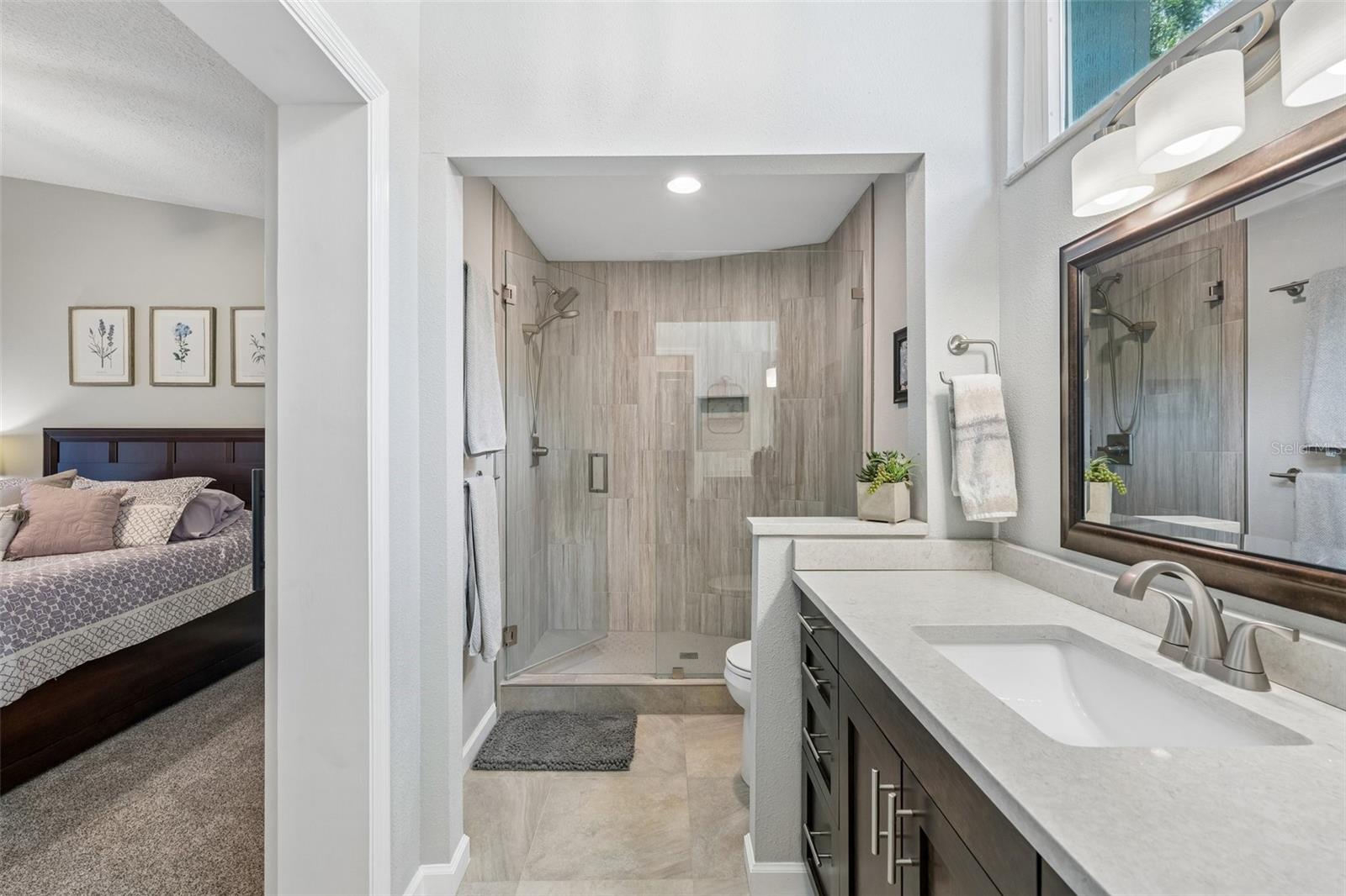 The primary bedroom is set on its own side of the home with vaulted ceilings, French doors to the patio, and an updated ensuite bath featuring a custom vanity, beautifully tiled glass-enclosed stand-up shower, high arched window, and walk-in closet with organized storage