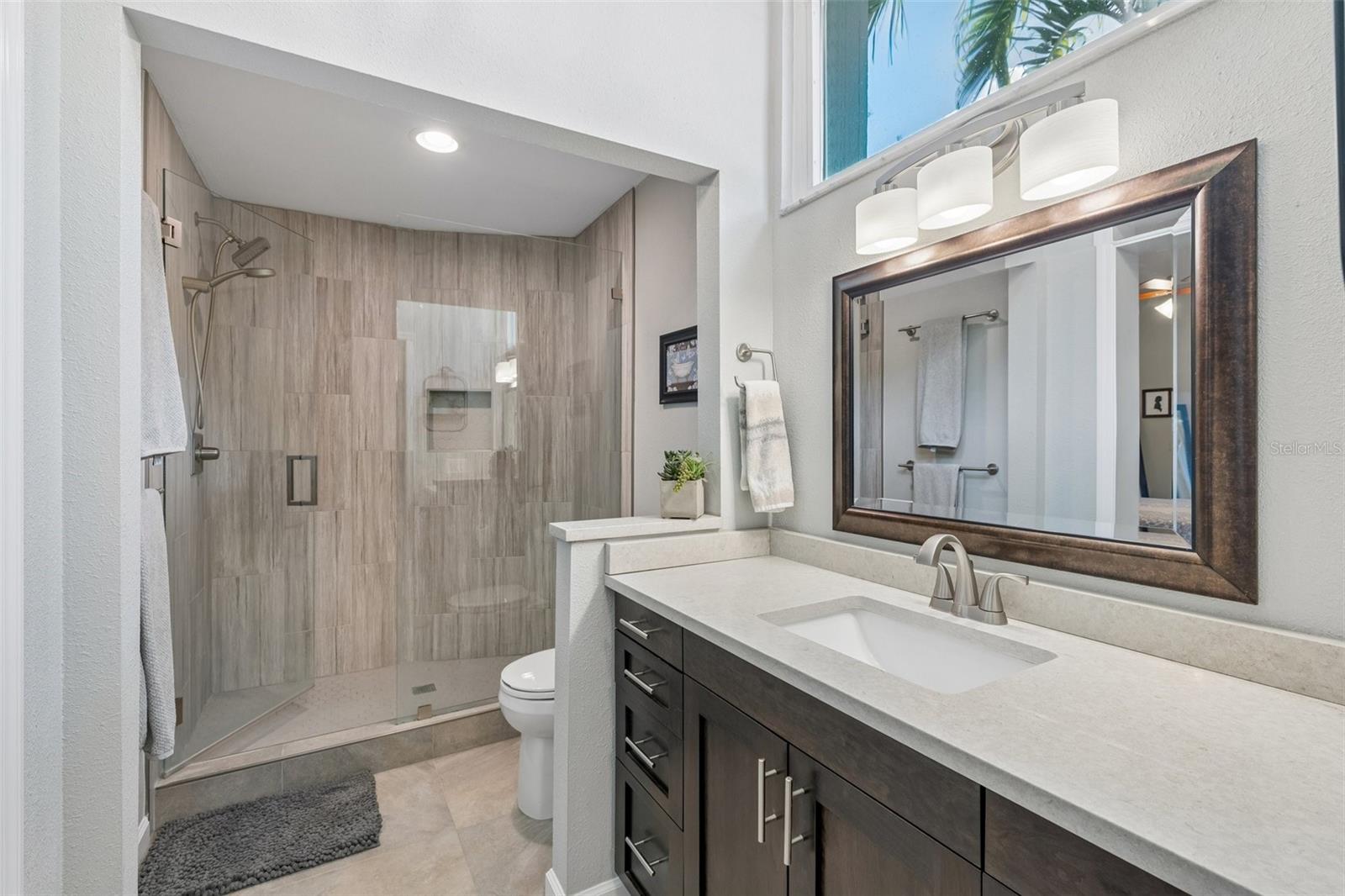 The primary bedroom is set on its own side of the home with vaulted ceilings, French doors to the patio, and an updated ensuite bath featuring a custom vanity, beautifully tiled glass-enclosed stand-up shower, high arched window, and walk-in closet with organized storage