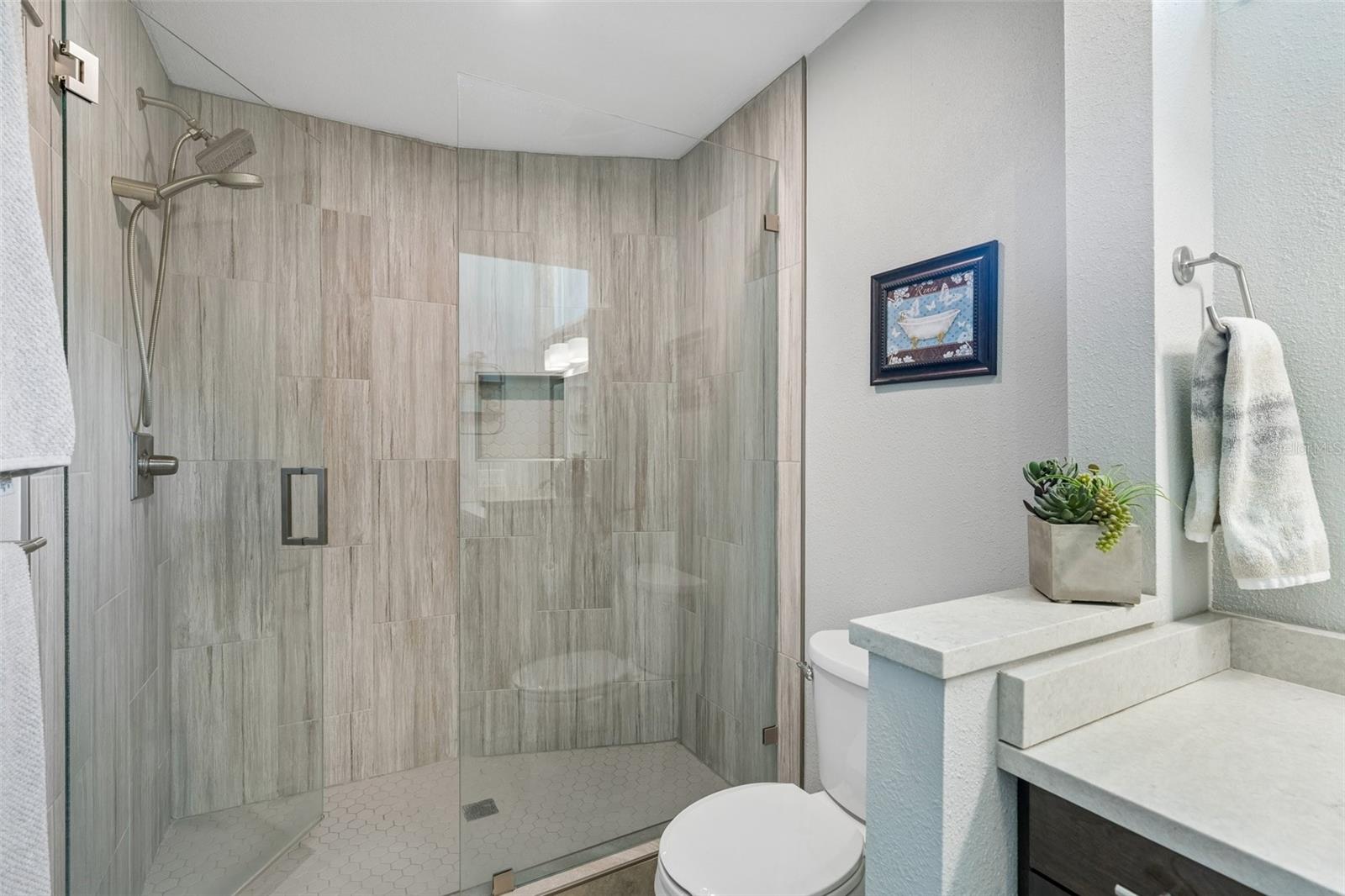 The primary bedroom is set on its own side of the home with vaulted ceilings, French doors to the patio, and an updated ensuite bath featuring a custom vanity, beautifully tiled glass-enclosed stand-up shower, high arched window, and walk-in closet with organized storage