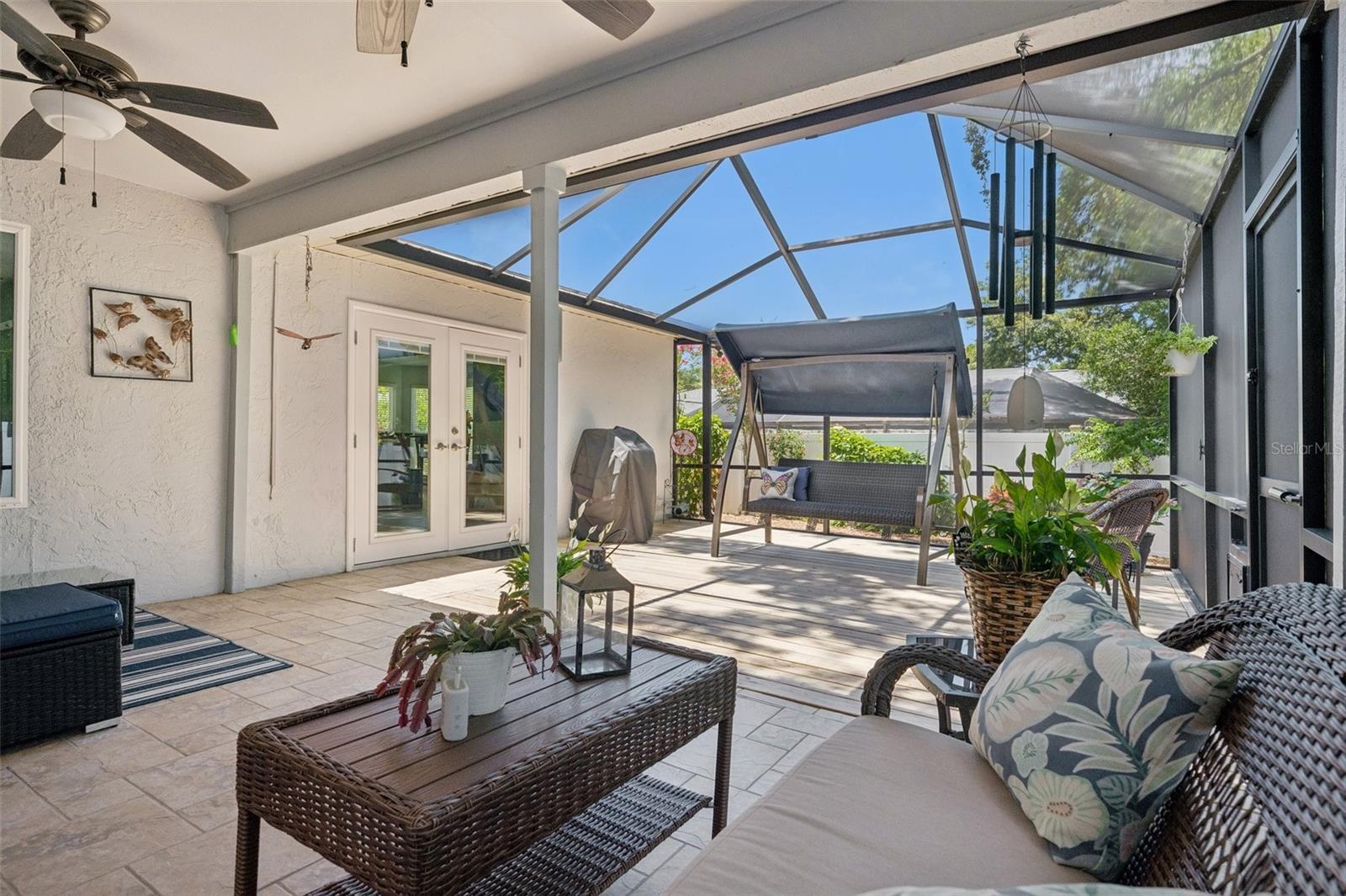 Oversized screened lanai featuring a covered seating area and wood deck, perfect for relaxing, dining, grilling, or enjoying peaceful evenings at home. Beyond the lanai, the xeriscaped backyard offers low-maintenance outdoor space with mature landscaping, tropical greenery, and a private fenced setting.
