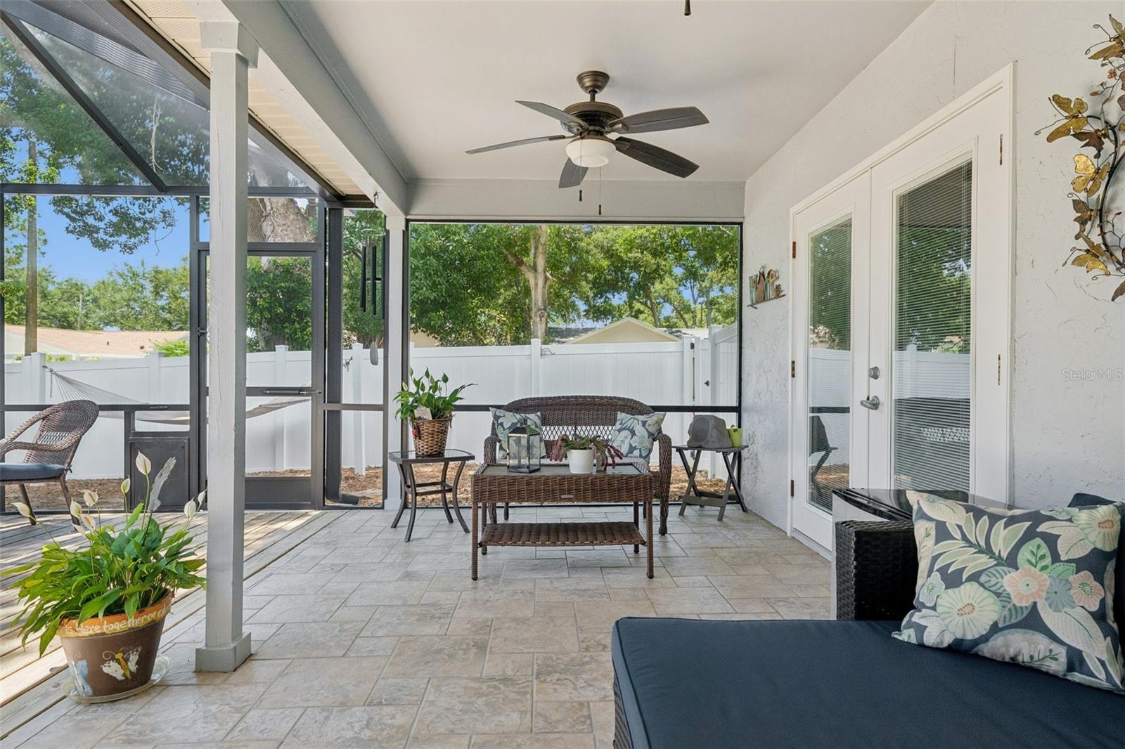 Oversized screened lanai featuring a covered seating area and wood deck, perfect for relaxing, dining, grilling, or enjoying peaceful evenings at home. Beyond the lanai, the xeriscaped backyard offers low-maintenance outdoor space with mature landscaping, tropical greenery, and a private fenced setting.