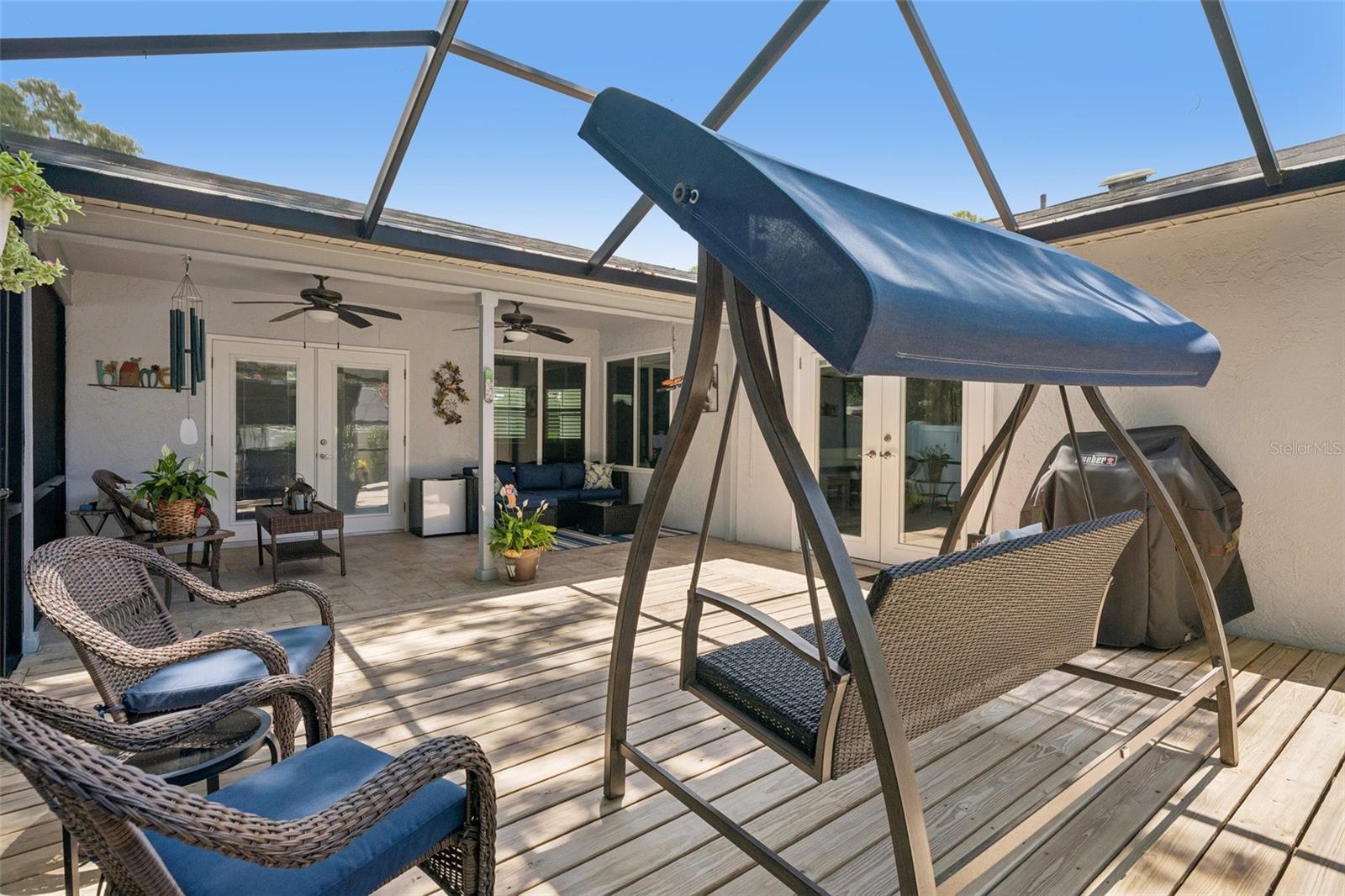 Oversized screened lanai featuring a covered seating area and wood deck, perfect for relaxing, dining, grilling, or enjoying peaceful evenings at home. Beyond the lanai, the xeriscaped backyard offers low-maintenance outdoor space with mature landscaping, tropical greenery, and a private fenced setting.
