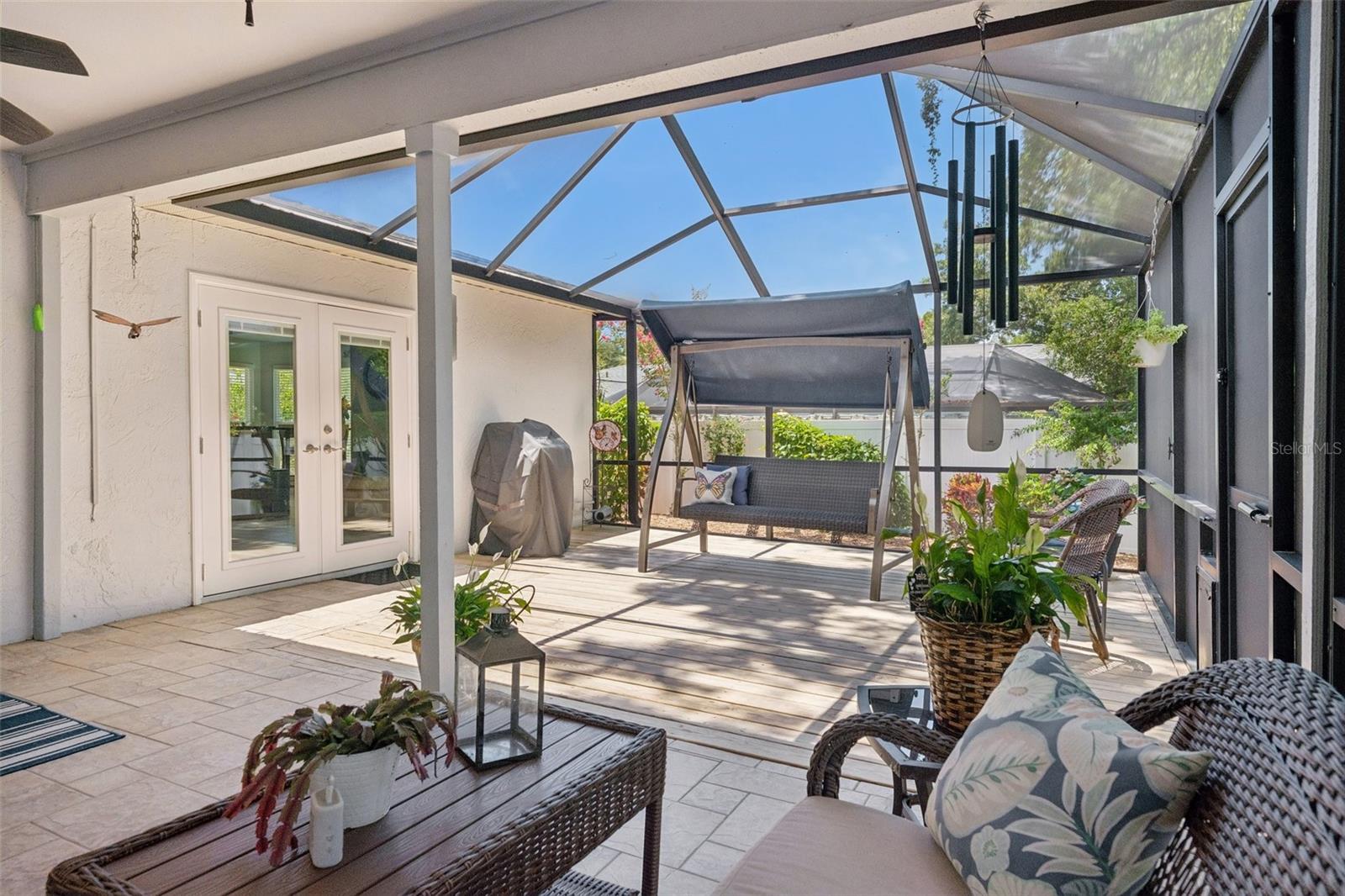 Oversized screened lanai featuring a covered seating area and wood deck, perfect for relaxing, dining, grilling, or enjoying peaceful evenings at home. Beyond the lanai, the xeriscaped backyard offers low-maintenance outdoor space with mature landscaping, tropical greenery, and a private fenced setting.