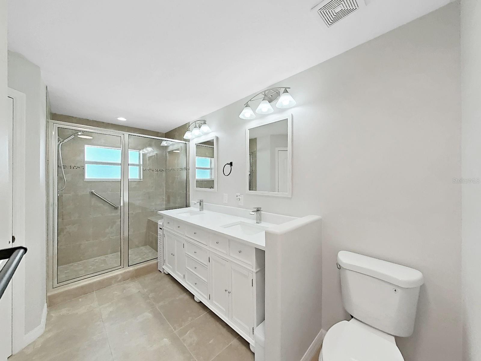 Primary En-suite bathroom.  Spacious shower has a nicely sized bench and stylish tile.  Vanity is new with double sinks. Linen closet and new toilet top it off!